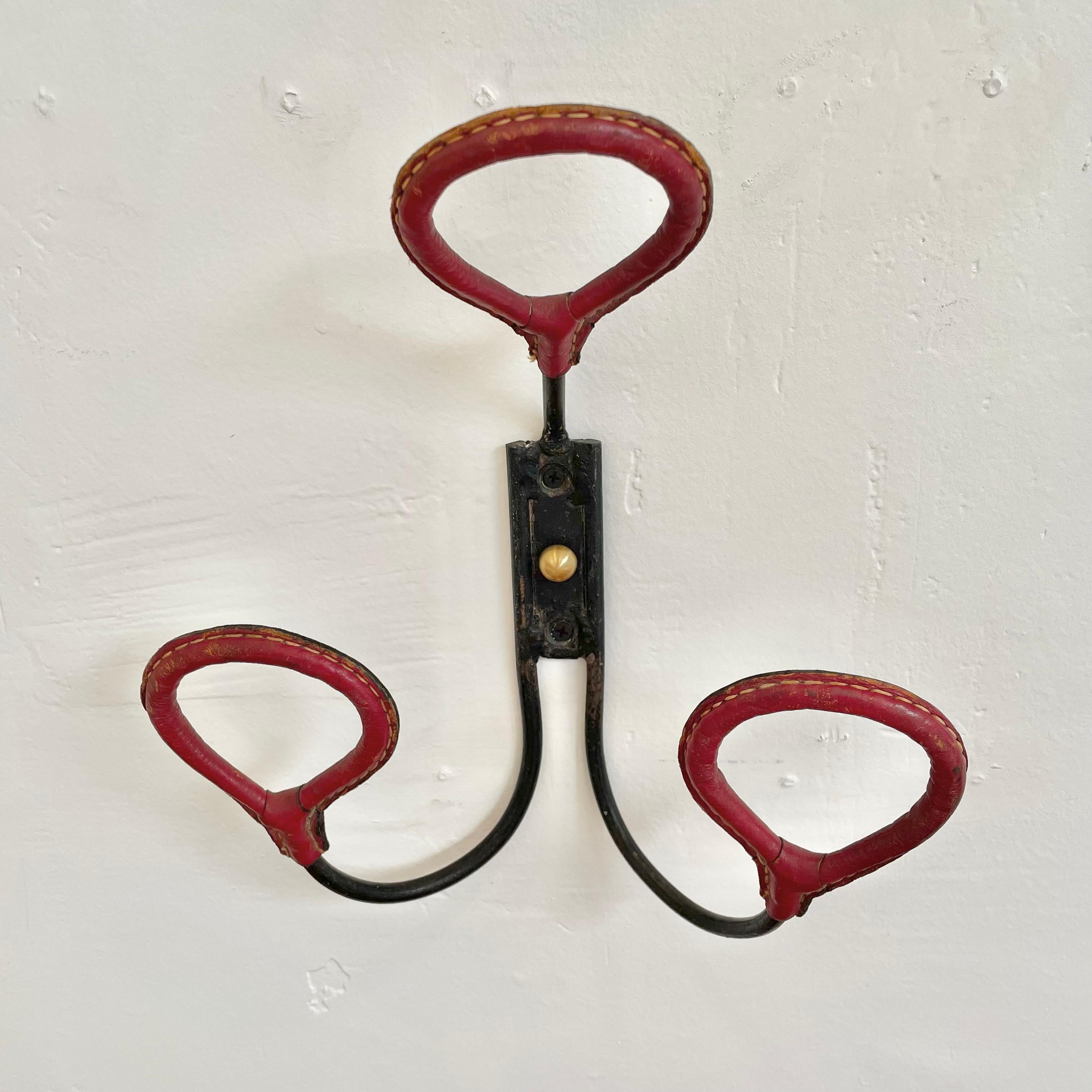 Handsome coat rack by Jacques Adnet. Iron frame with iron loop hooks wrapped in red saddle leather with signature Adnet contrast stitching. Good vintage condition. Fantastic piece of collectible Adnet.

