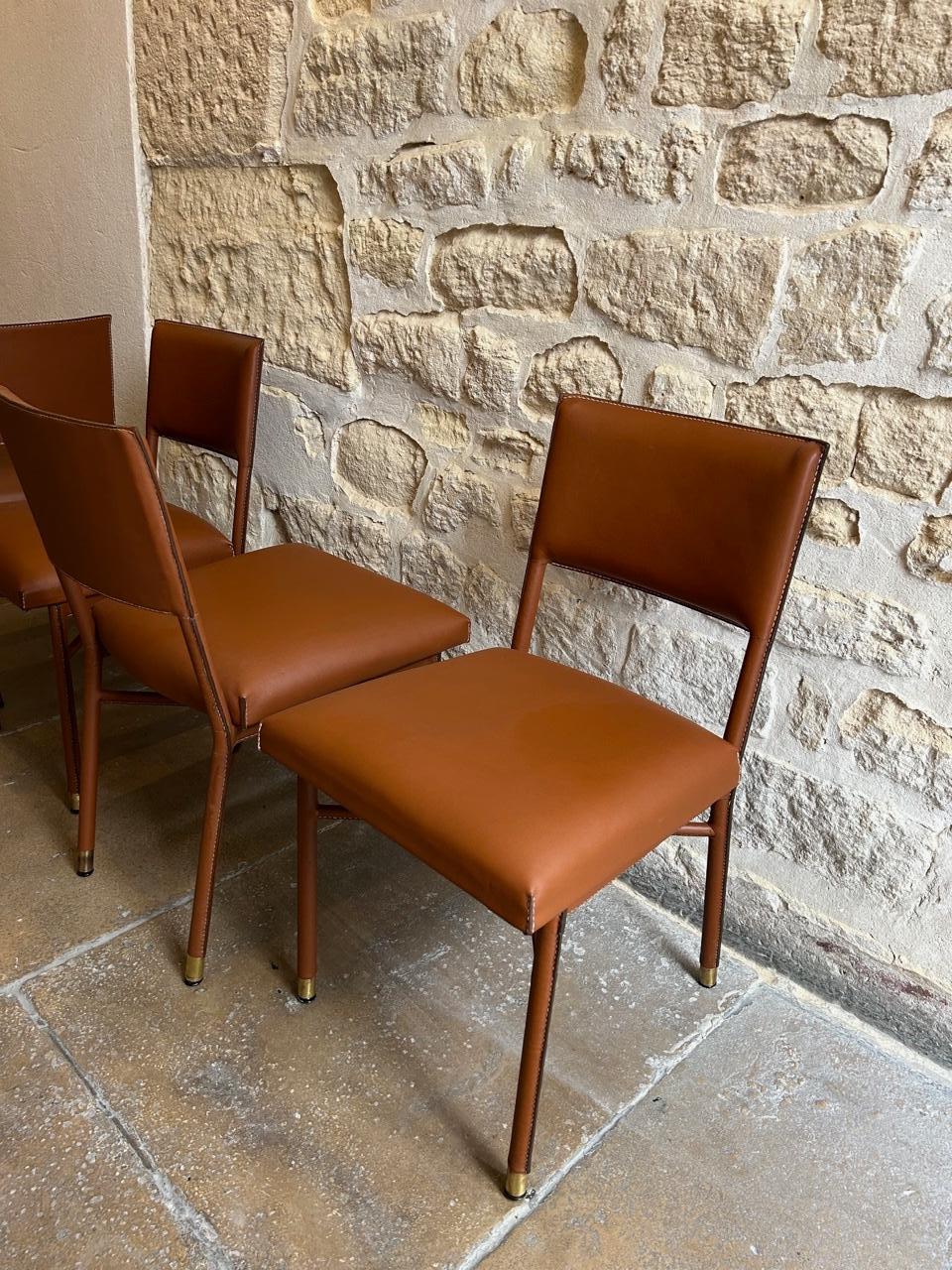 Elegante set di quattro sedie Jacques Adnet rivestite in pelle piqué-sellier cucita a mano.