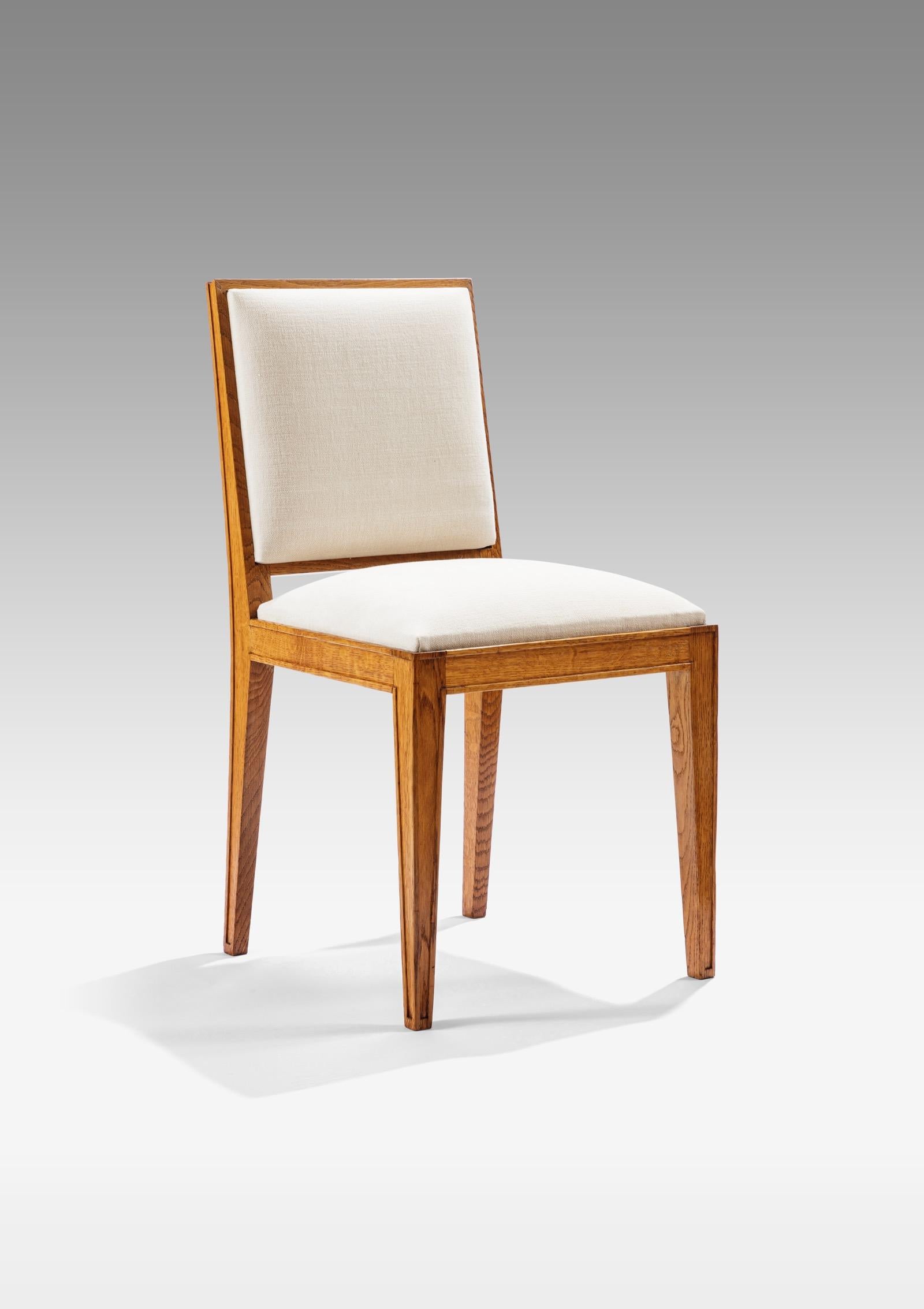 Set of six oak chairs with slightly inclined backs and tapered legs, back and seats covered with cream fabric.