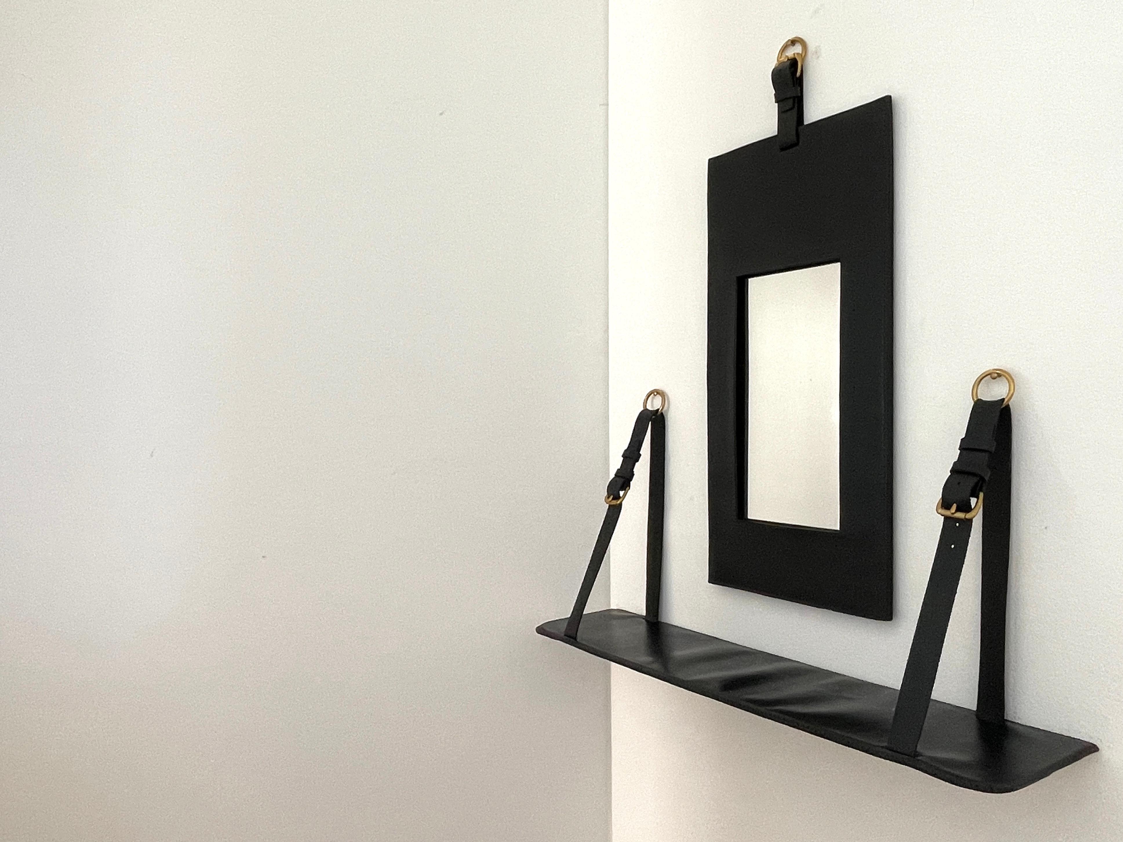 Jacques Adnet mirror and wall shelf.
Black leather framed mirror with black leather floating shelf.
Brass hardware.

Mirror - 11