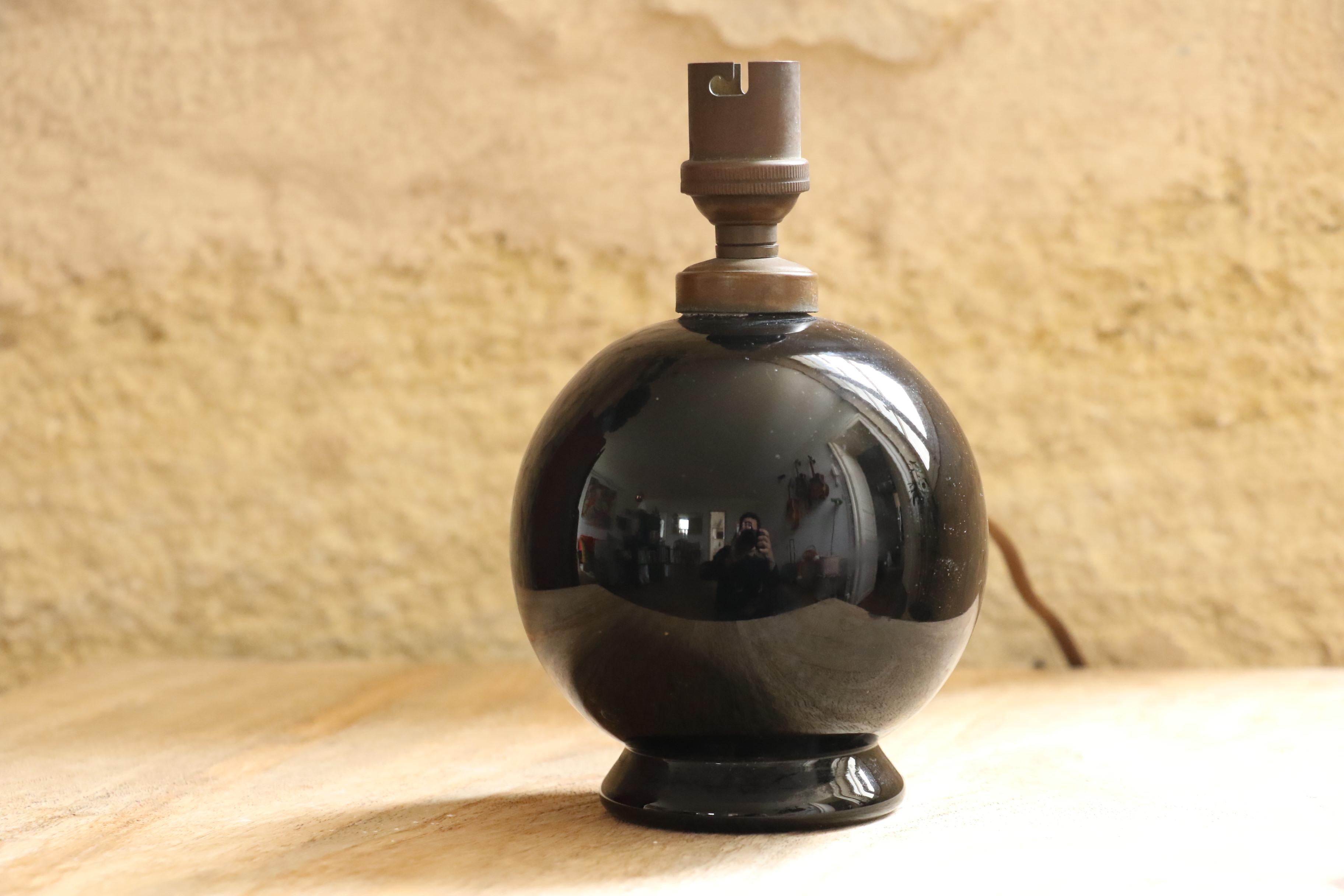 Elegant and rare black lacquered glass table lamp designed by Jacques Adnet in the 1950s. This spherical lamp sits on a small pedestal base, creating a refined and timeless silhouette. The deep black lacquered glass reflects light beautifully,