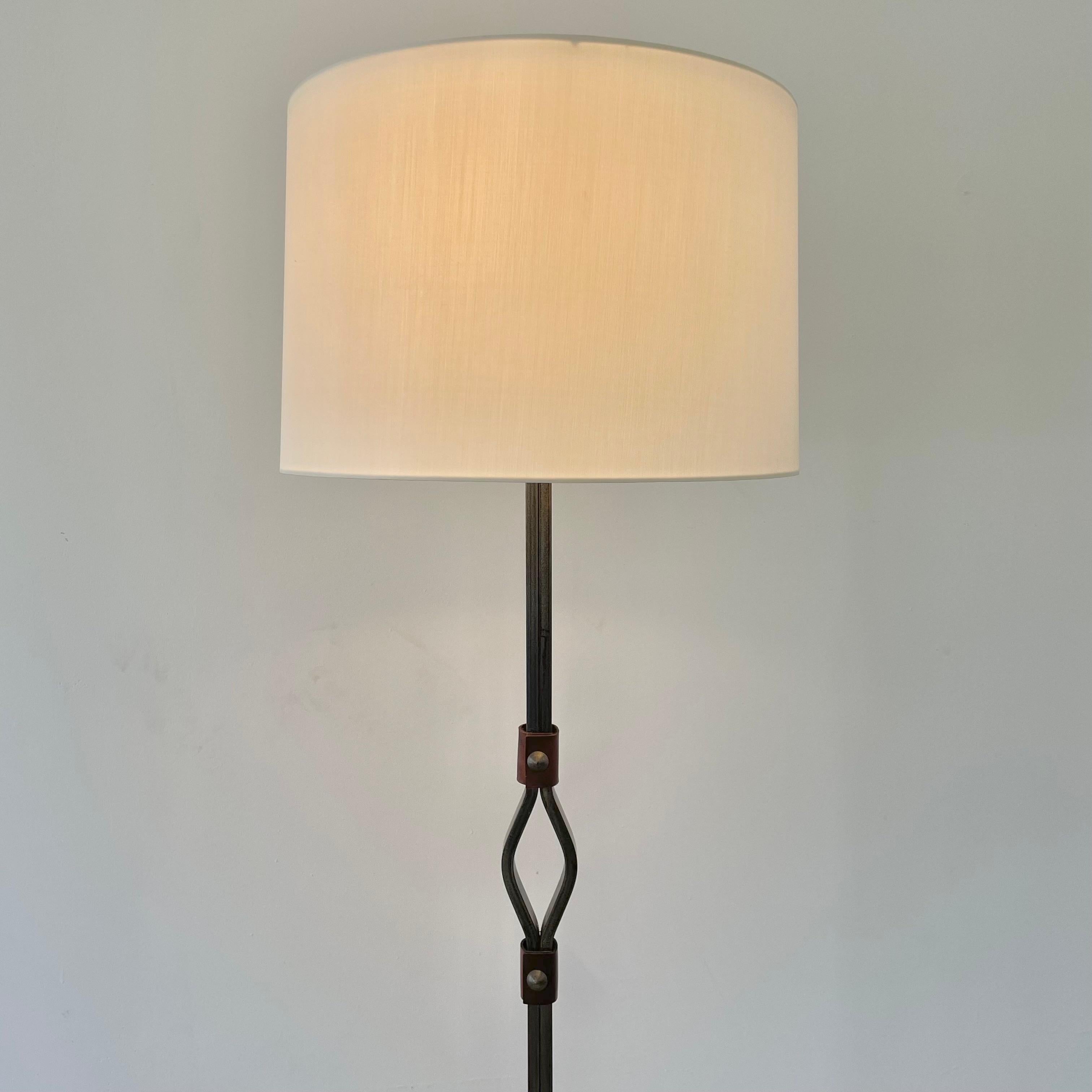 Stunning steel floor lamp by French modernist designer Jacques Adnet. Made in France in the 1950s. Horseshoe shaped base with with thick steel frame. Thick saddle leather accents wrap around the frame in five locations; two at the base, and three