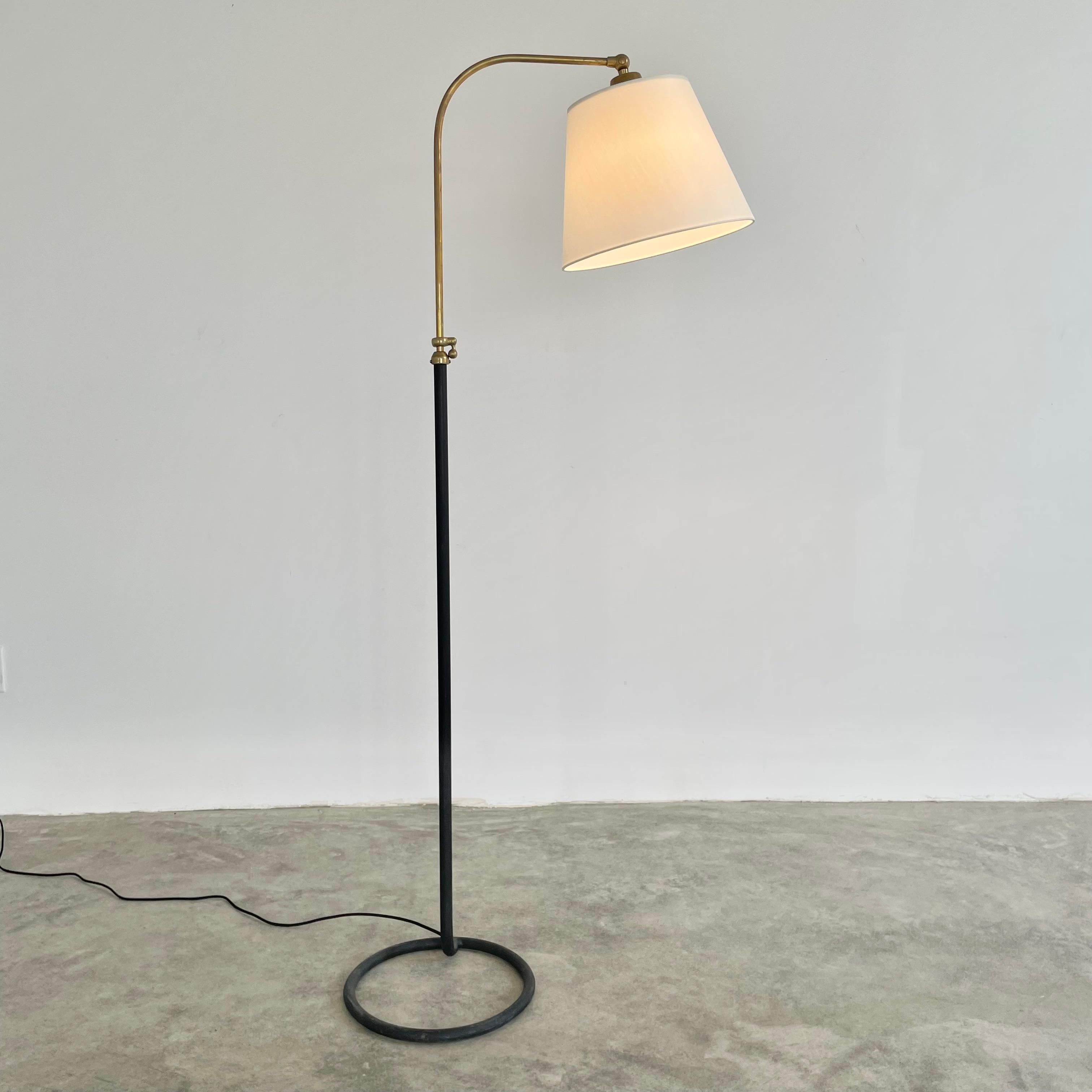 Handsome brass and metal floor lamp in the style of French designer Jacques Adnet. Circa 1950s. Circular metal base and stem are one solid piece. Height adjustable curved brass rod. New custom fitted silk shade and light diffusor. Beautiful