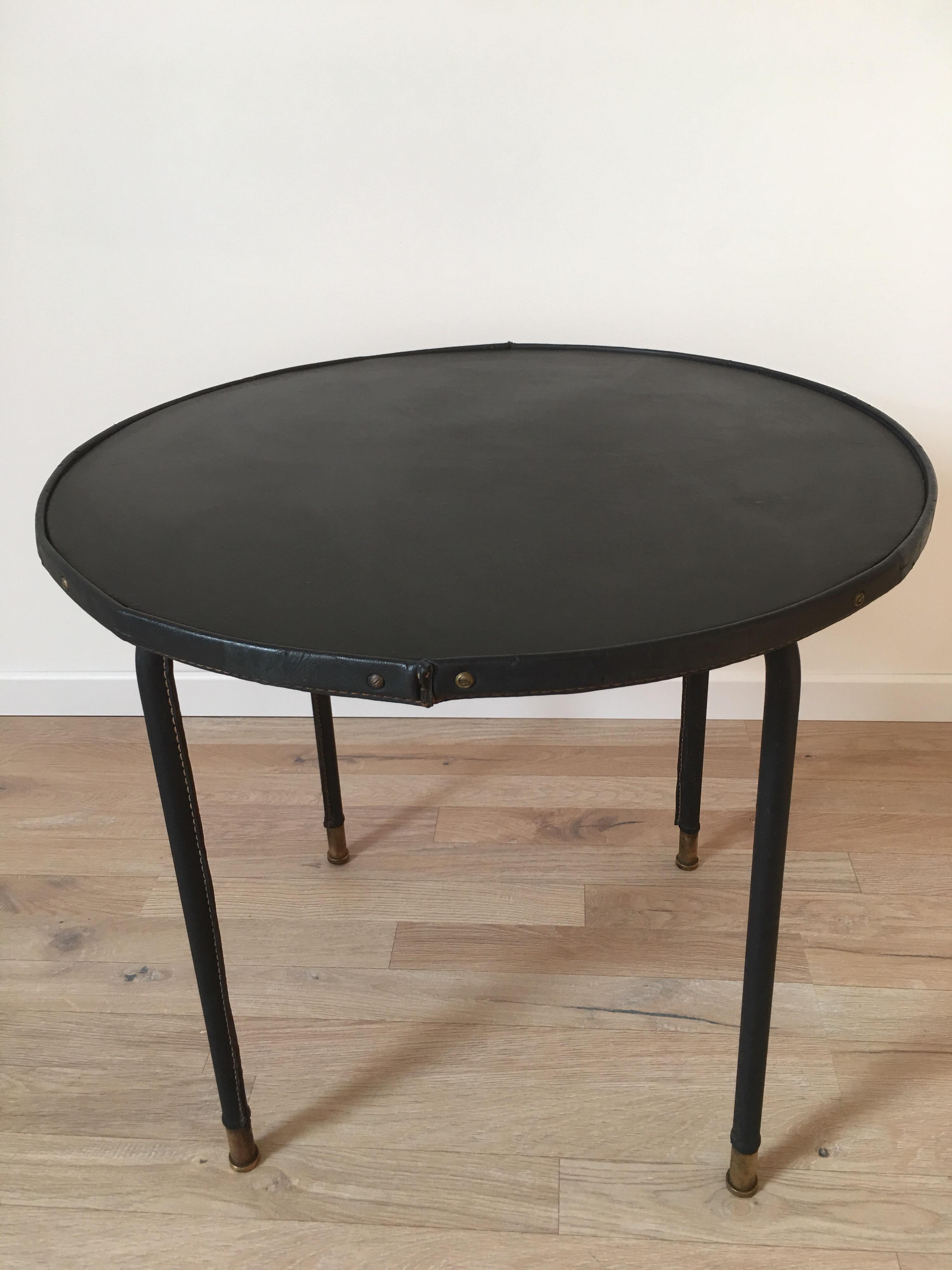 Black stitched leather side table designed in the 1950s.
The round top is based on 4 black leather-clad feet ending in bronze clogs. The previous owner changed the leather of the tray 20 years ago
The table is in good condition with a vintage patina