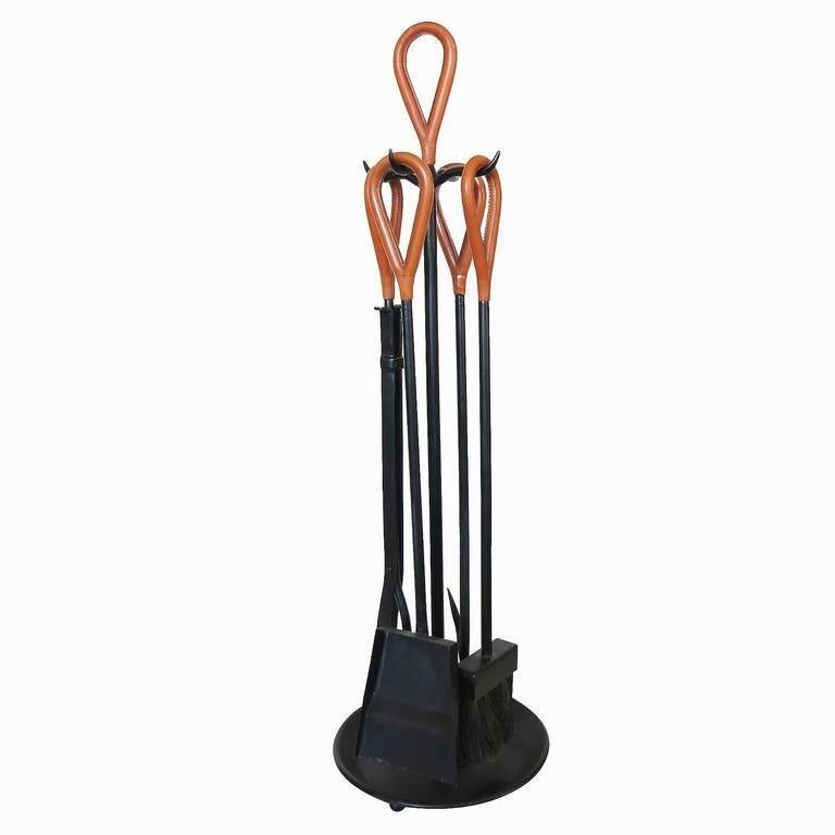 Jacques Adnet style fire tools with handstitched leather handles atop wrought iron.

This set includes a stand, long tongs, poker, brush and shovel.
