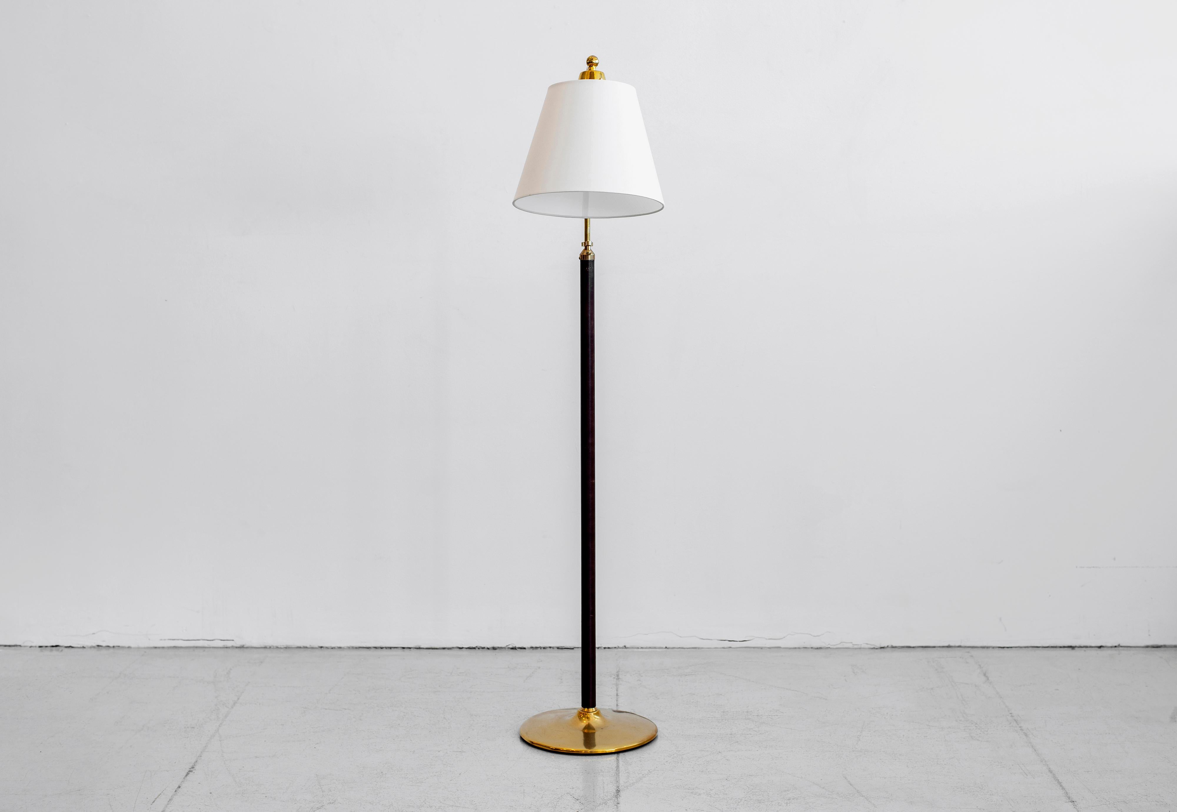 Handsome French floor lamp in the style of Jacques Adnet. Brass stem wrapped in dark brown leather with contrast stitching and brass disc base. Great age and patina. Shade pivots and brass neck is height adjustable. Newly re-wired with new shade.