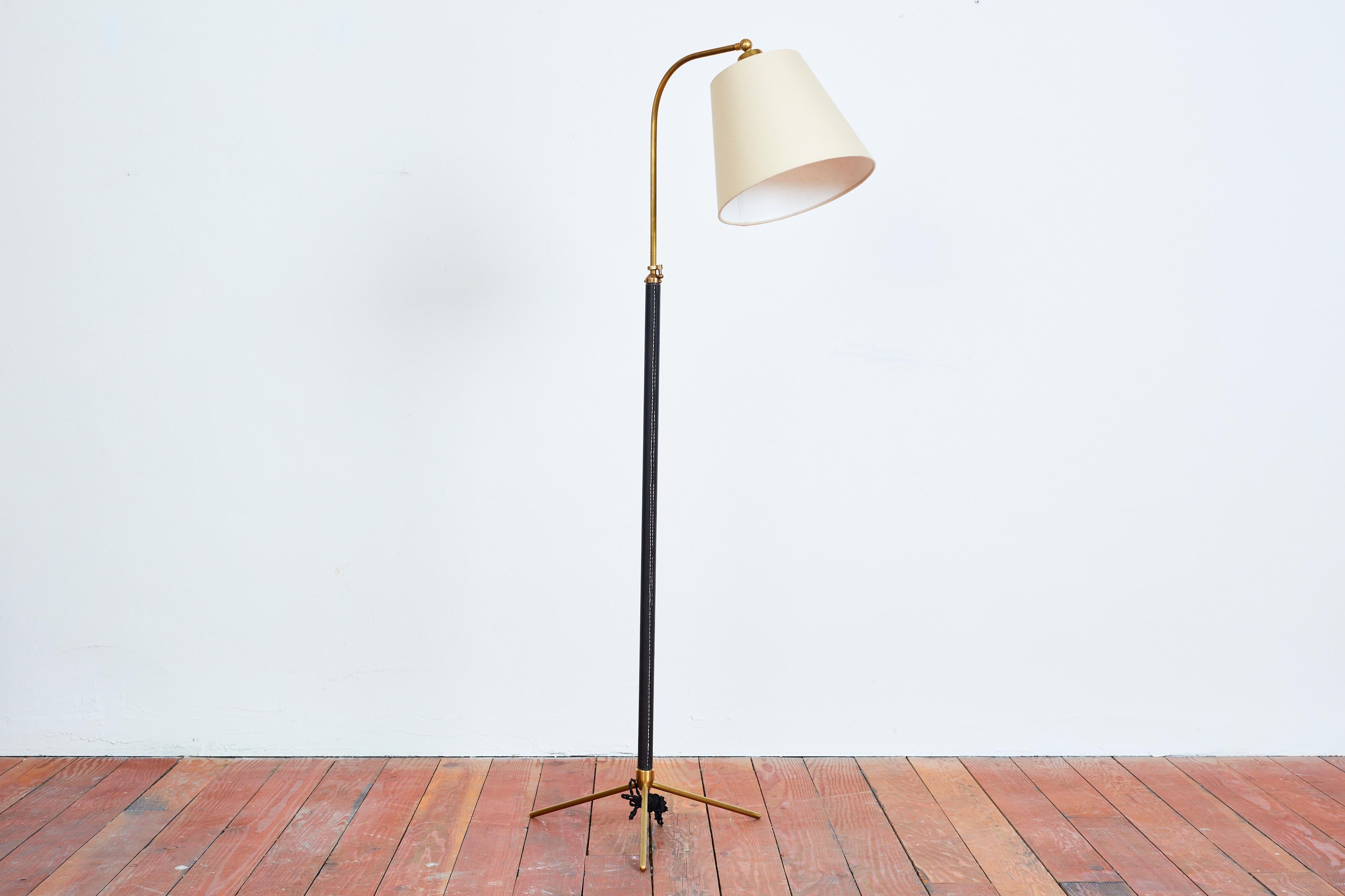 Handsome French floor lamp attributed to Jacques Adnet with hand-stitched black leather, contrast stitching, brass tripod base and new silk shade. 
Newly rewired. 
Height extends from 48” - 64.5”.