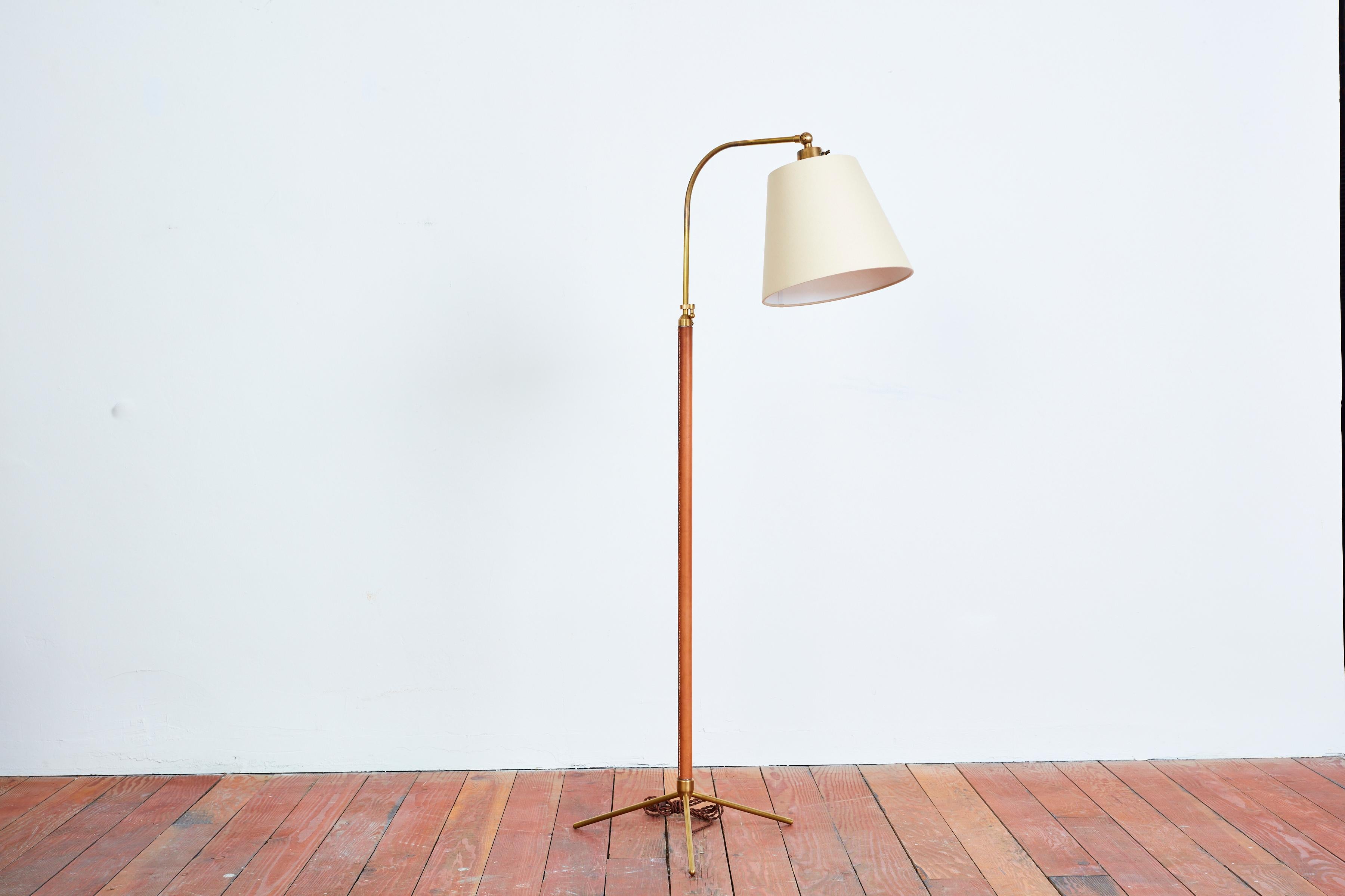 Handsome French floor lamp by Jacques Adnet with hand-stitched camel brown leather, contrast stitching, brass tripod base and new silk shade. 
Newly rewired. 
Height extends from 48” - 64.5”.