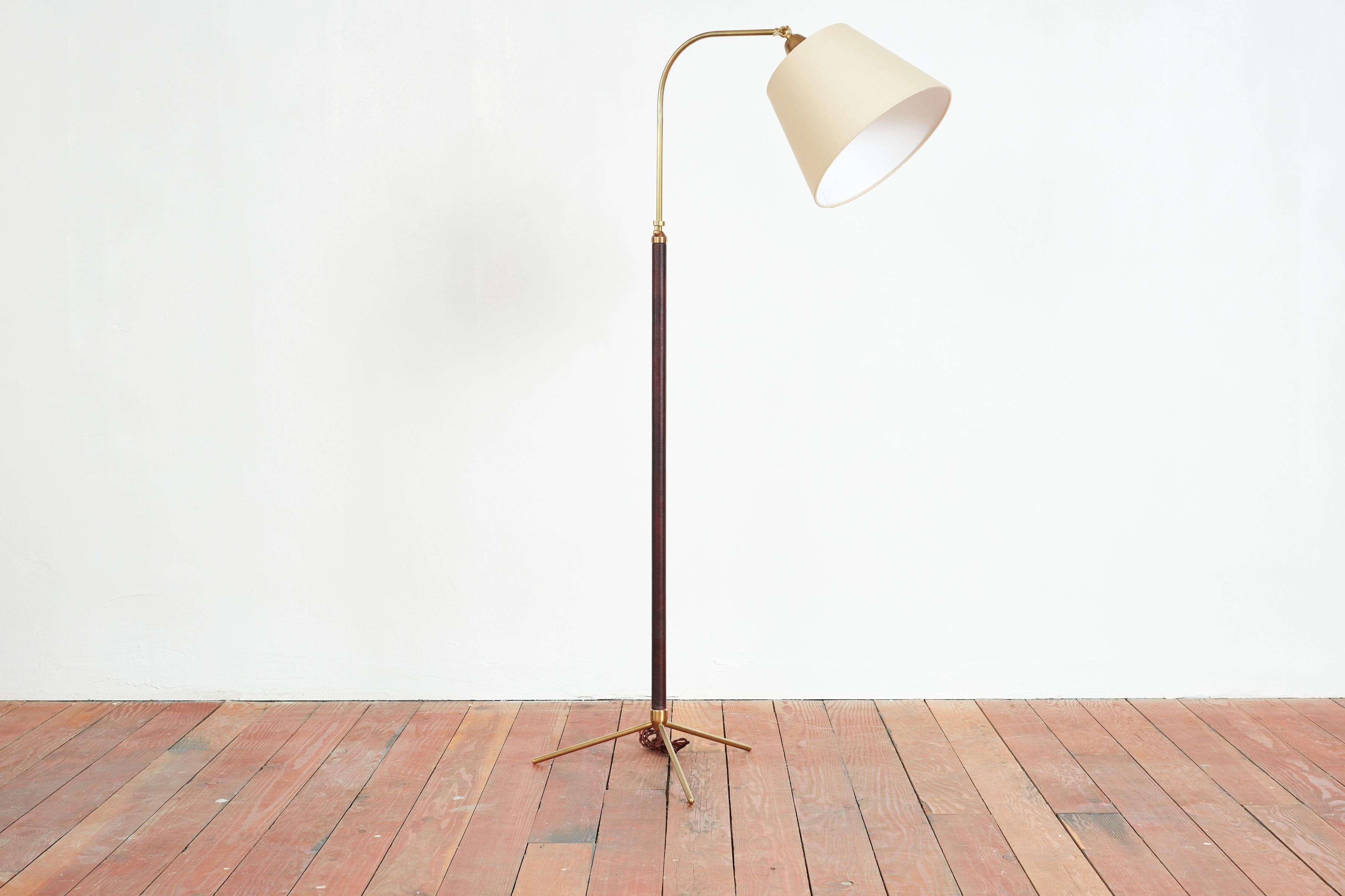 Burgandy Leather floor lamp attributed to Jacques Adnet with polished brass tripod base and brass hardware.
 Adjustable height mechanism 
New linen shade 
Lamp Height 54