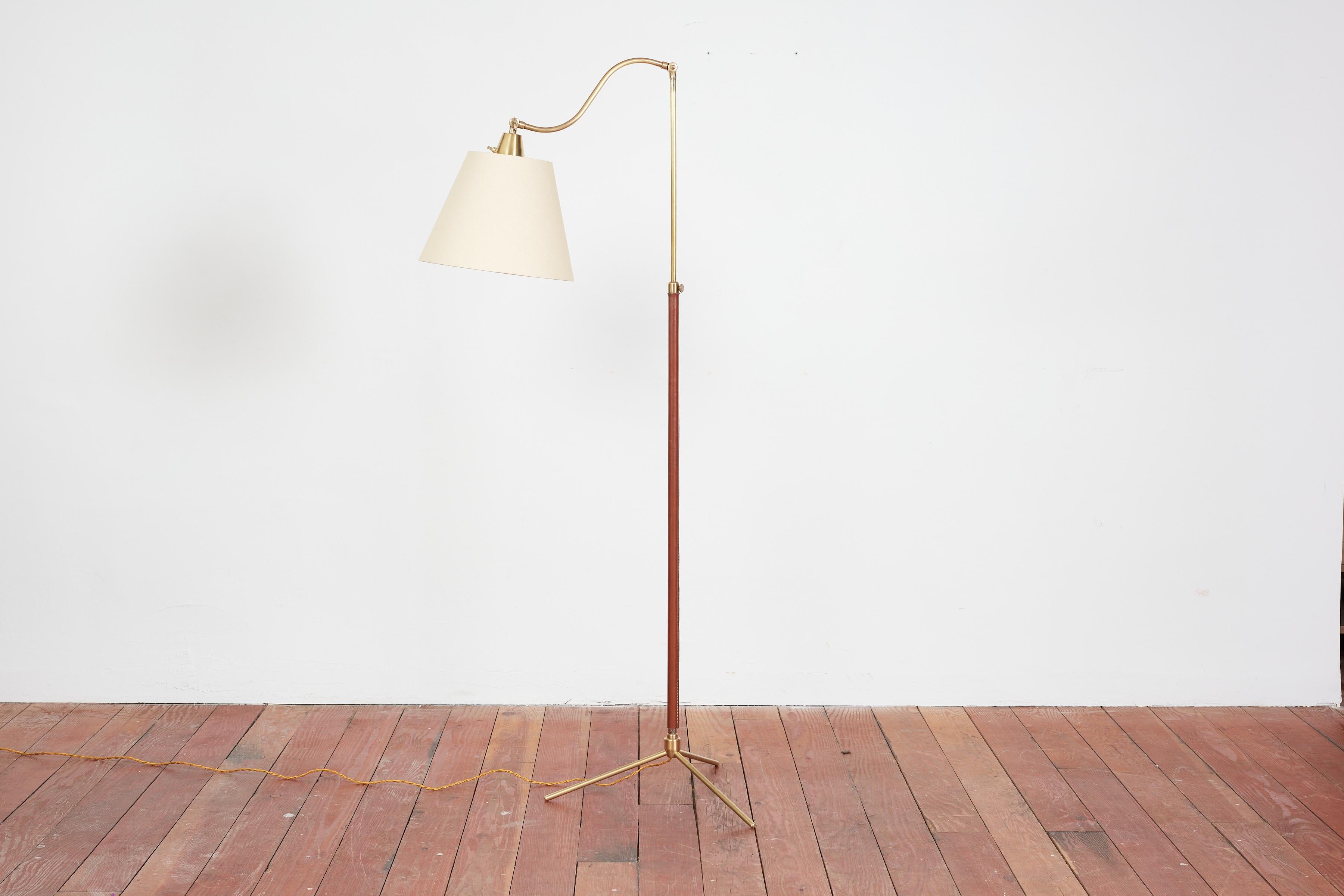 Handsome French floor lamp by Jacques Adnet with hand-stitched camel brown leather, contrast stitching, brass tripod base and new linen shade. 

Newly rewired.

 Height extends from 65” - 76”.