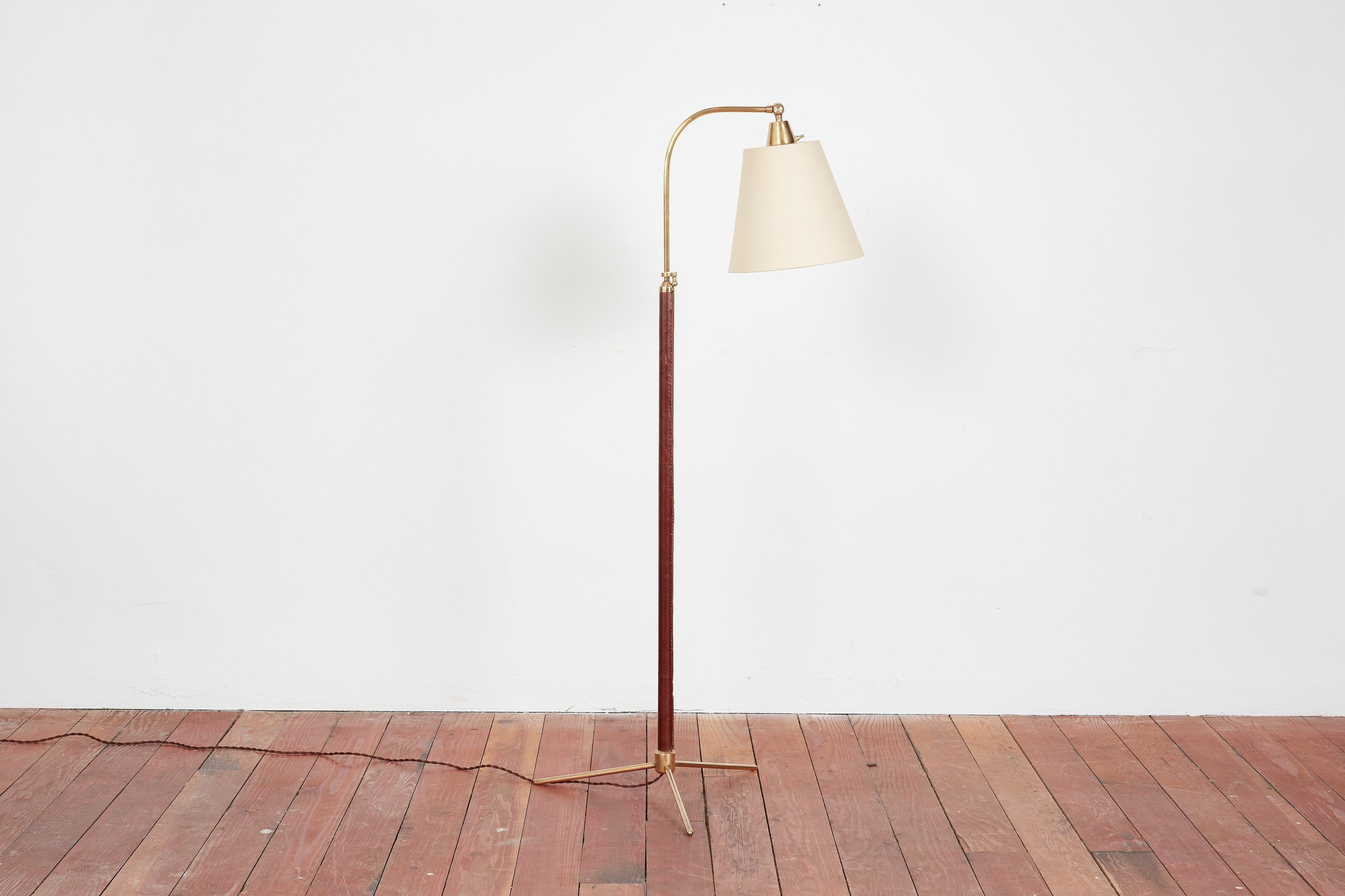 Handsome French floor lamp by Jacques Adnet with hand-stitched dark brown leather, contrast stitching, brass tripod base and new linen shade.

Newly rewired. 

Height extends from 48” - 64.5”.