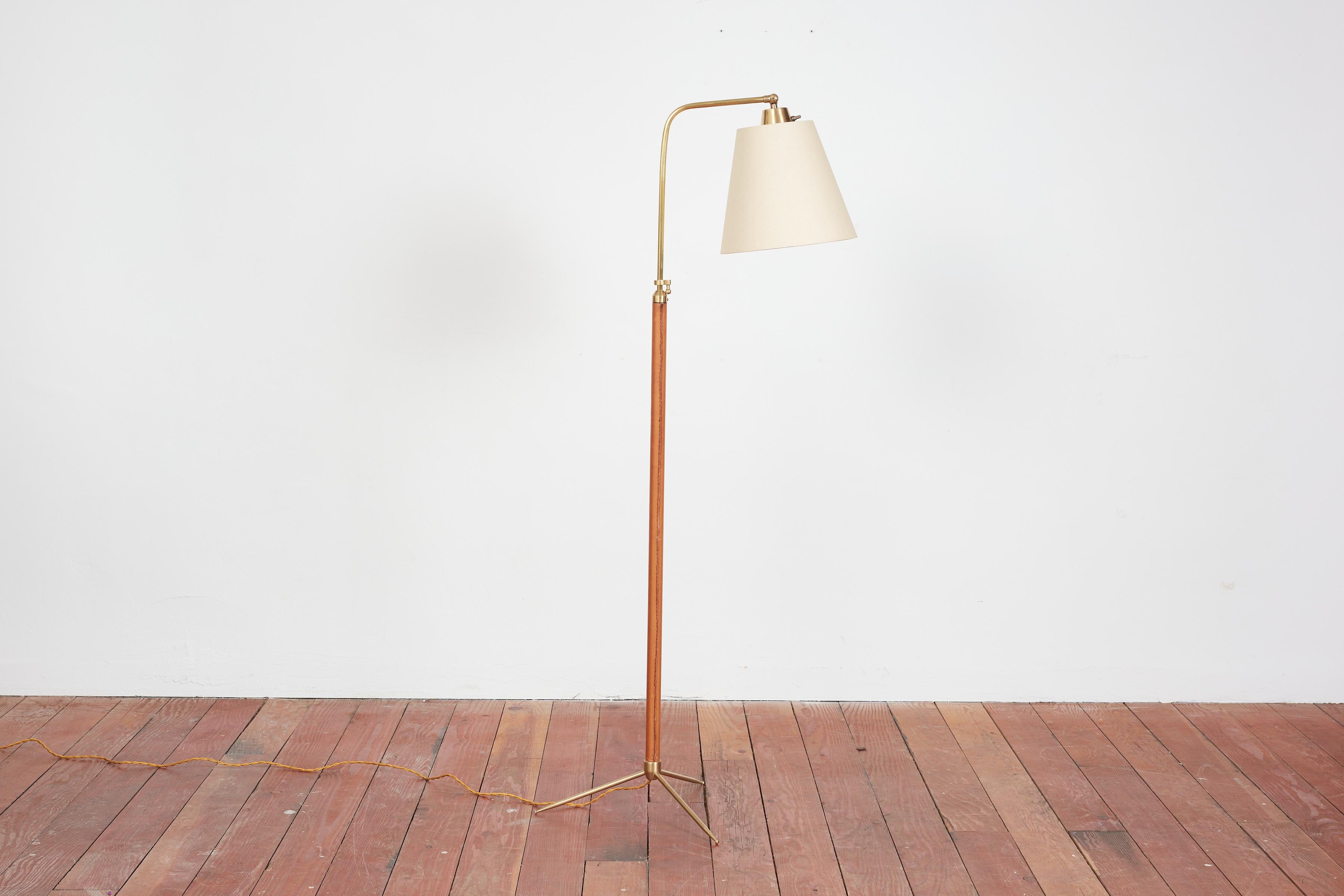 Handsome French floor lamp by Jacques Adnet with hand-stitched camel brown leather, contrast stitching, brass tripod base and new silk shade. 

Newly rewired.

Height extends from 48” - 64.5”.