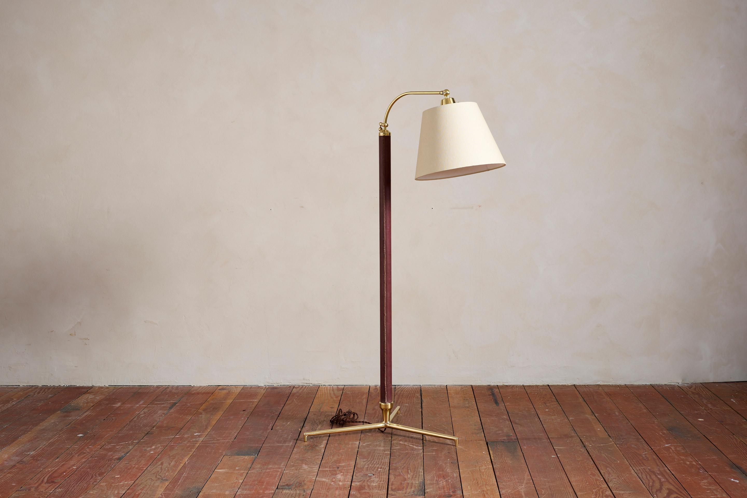 Handsome French floor lamp by Jacques Adnet with hand-stitched burgundy chocolate colored leather, contrast stitching, brass tripod base and new linen articulating shade

Newly rewired.

Height extends from 57” - 73”.