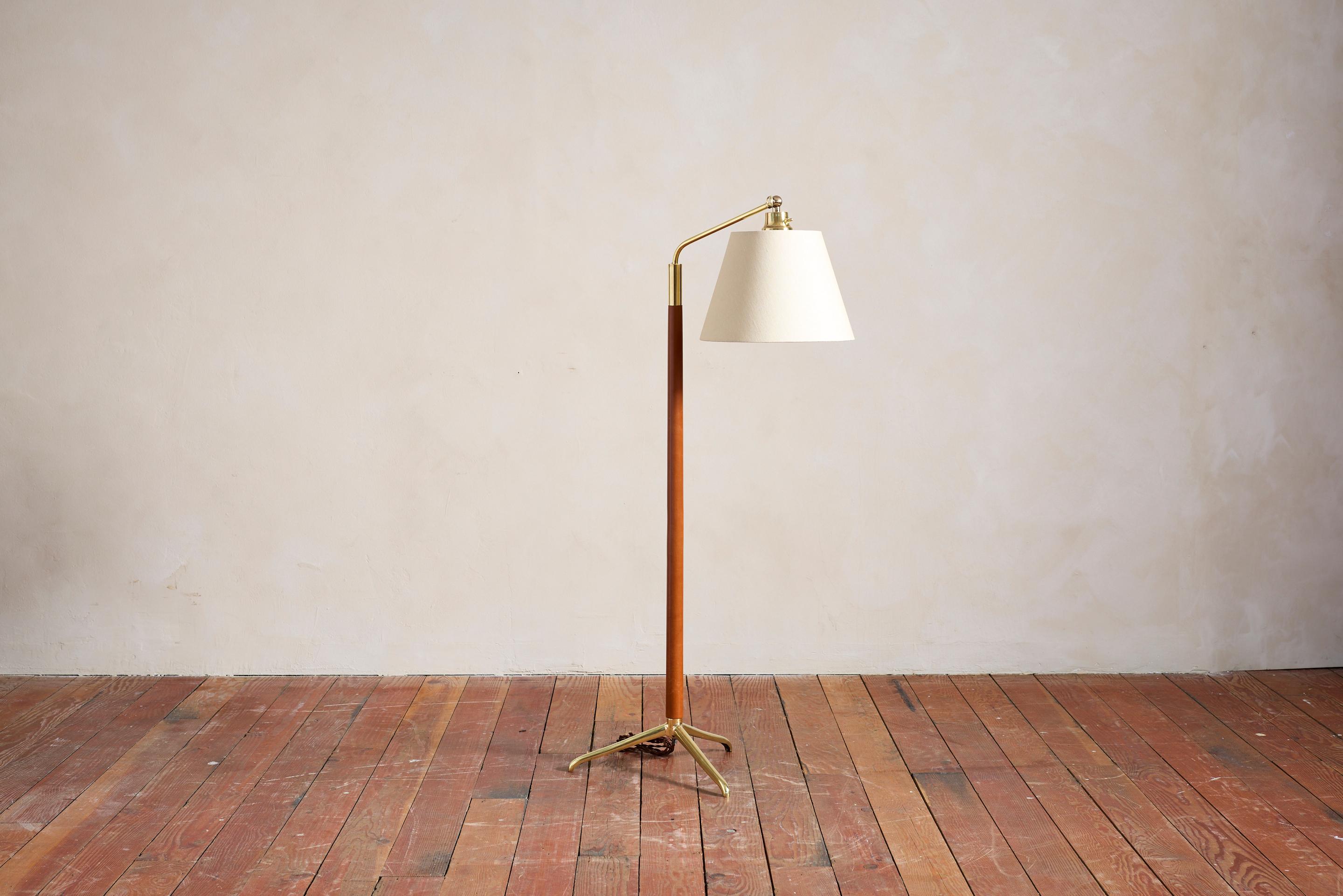 Handsome French floor lamp attributed to Jacques Adnet with hand-stitched camel brown leather, contrast stitching, polished solid brass tripod base and new silk shade. 

Newly rewired.

Height extends from 54.5” - 64.5”.