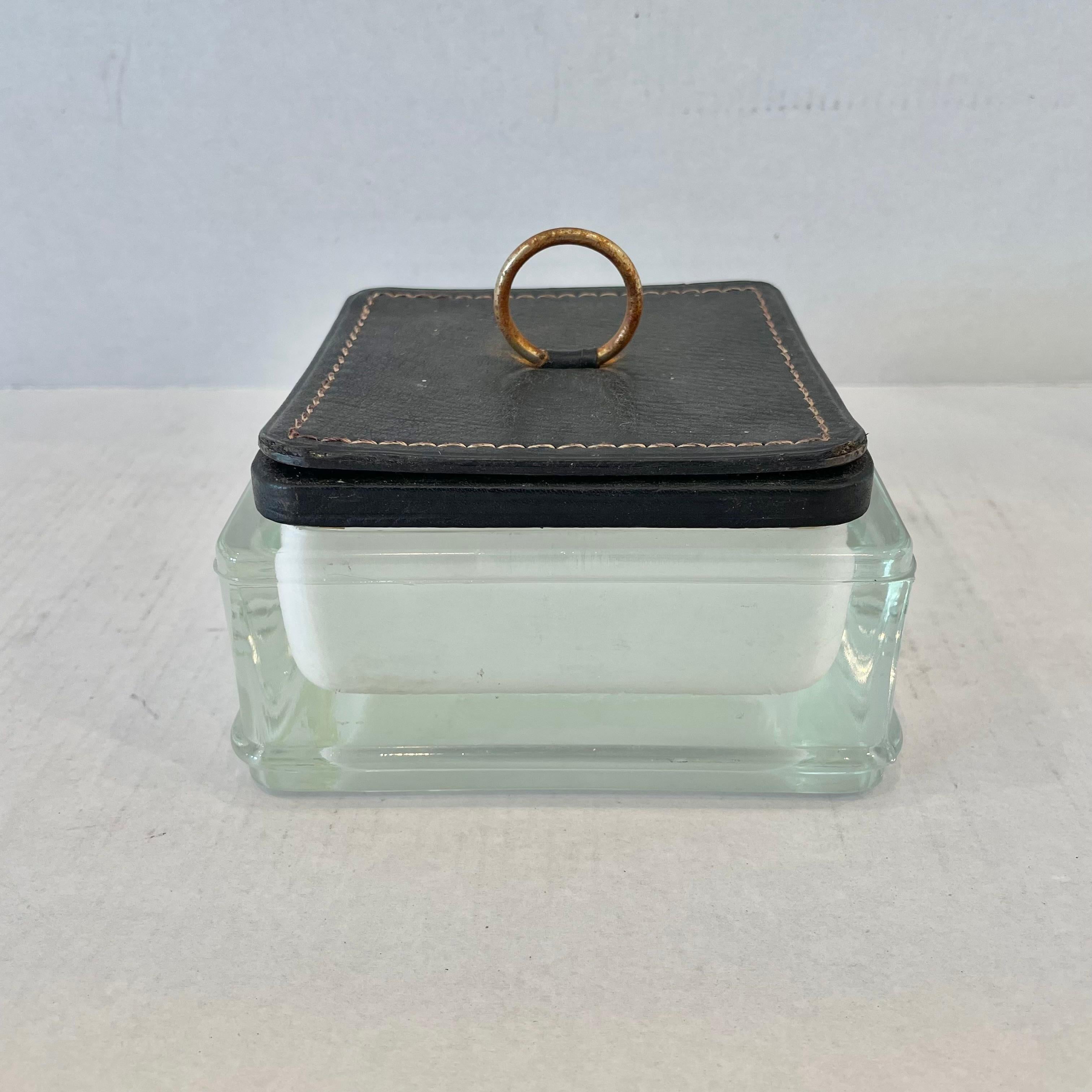 Substantial glass catchall / ashtray  with a leather lid in the style of French designer Jacques Adnet. Thick frosted glass body with a lid made of black leather with contrast stitching around the edges. Lid also features a metal ring attached to