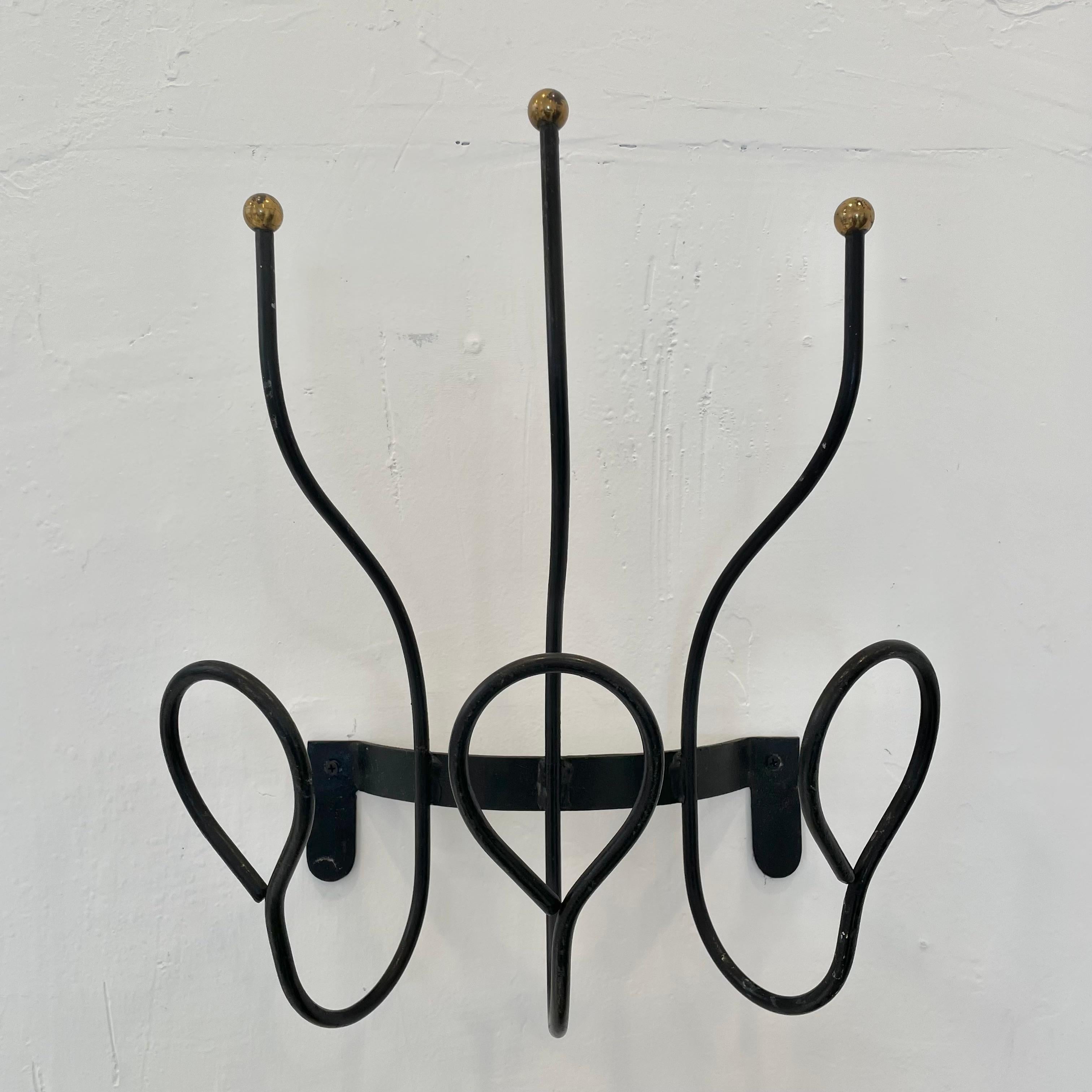 Handsome iron wall rack in the style of French designer Jacques Adnet. Good vintage condition. Iron frame with brass ball detailing at the top of each hook. Three tongue hooks along the bottom and three prong hooks at the top giving this piece a
