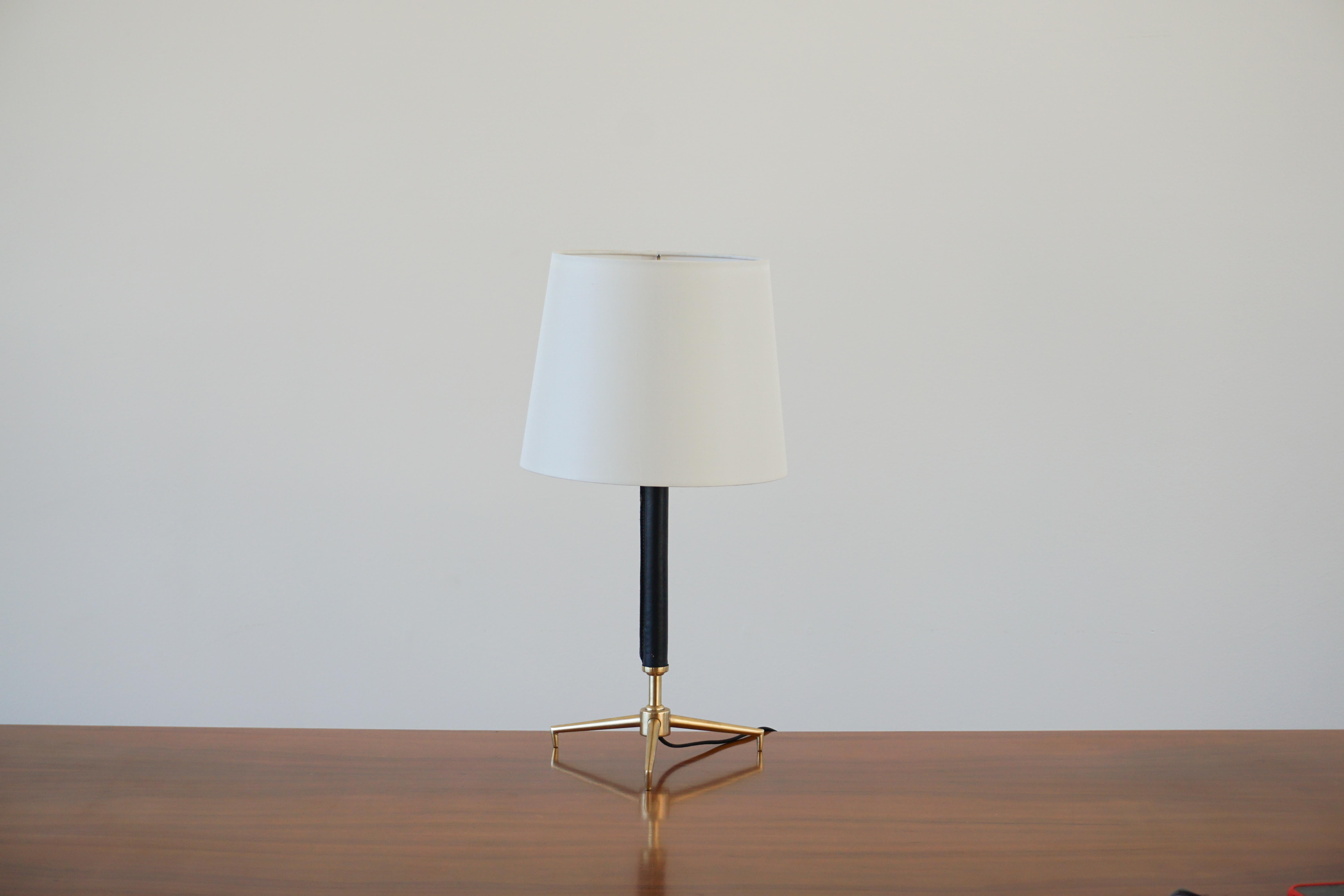 Petite French desk lamp in the style of Jacques Adnet. 
Brass tripod base with black leather and signature stitching. 
Great scale. 
Newly rewired with new shade.
 