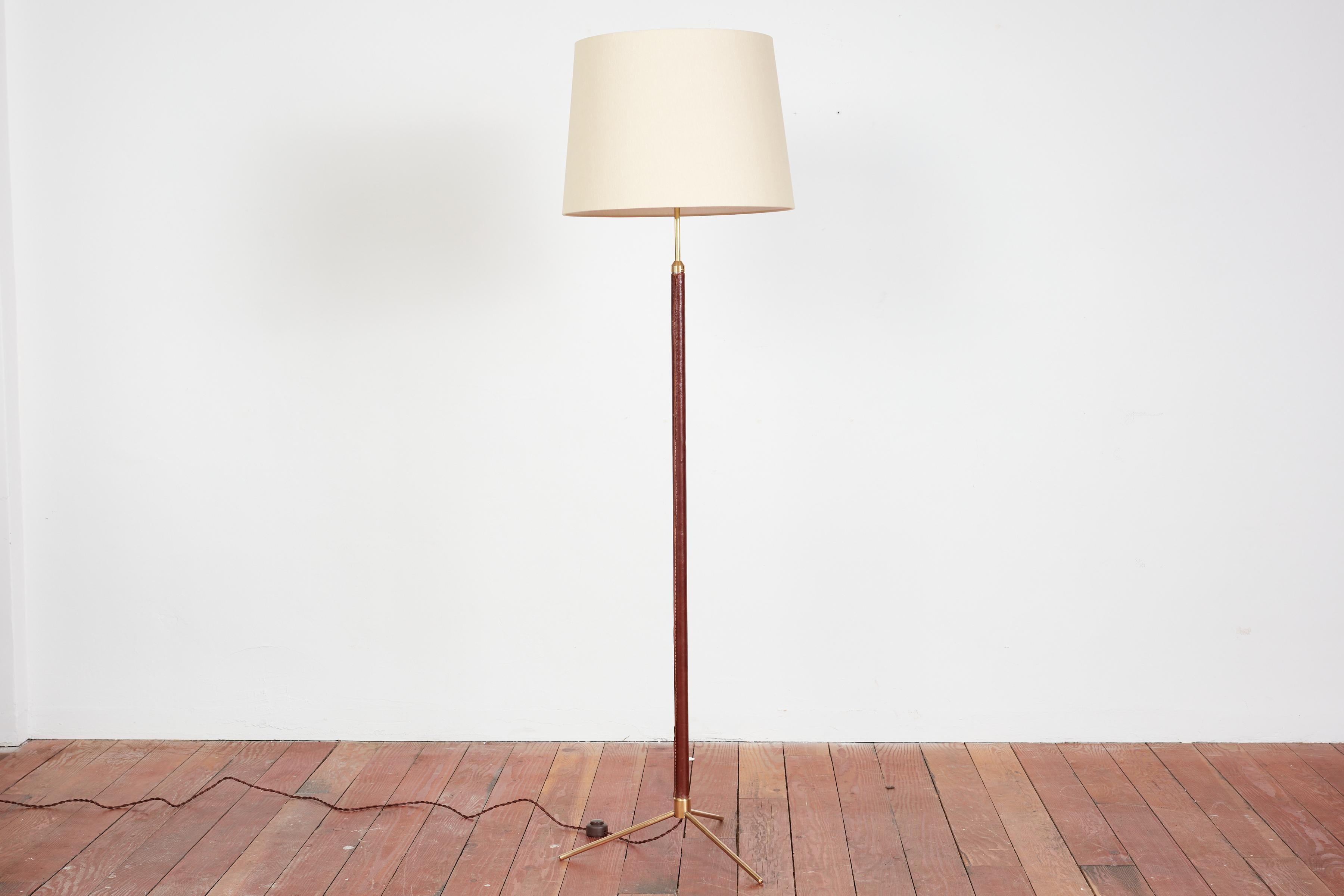 Handsome French floor lamp by Jacques Adnet.

Signature hand-stitched dark brown leather, contrast stitching, brass tripod base and new silk shade. 

Newly rewired. 