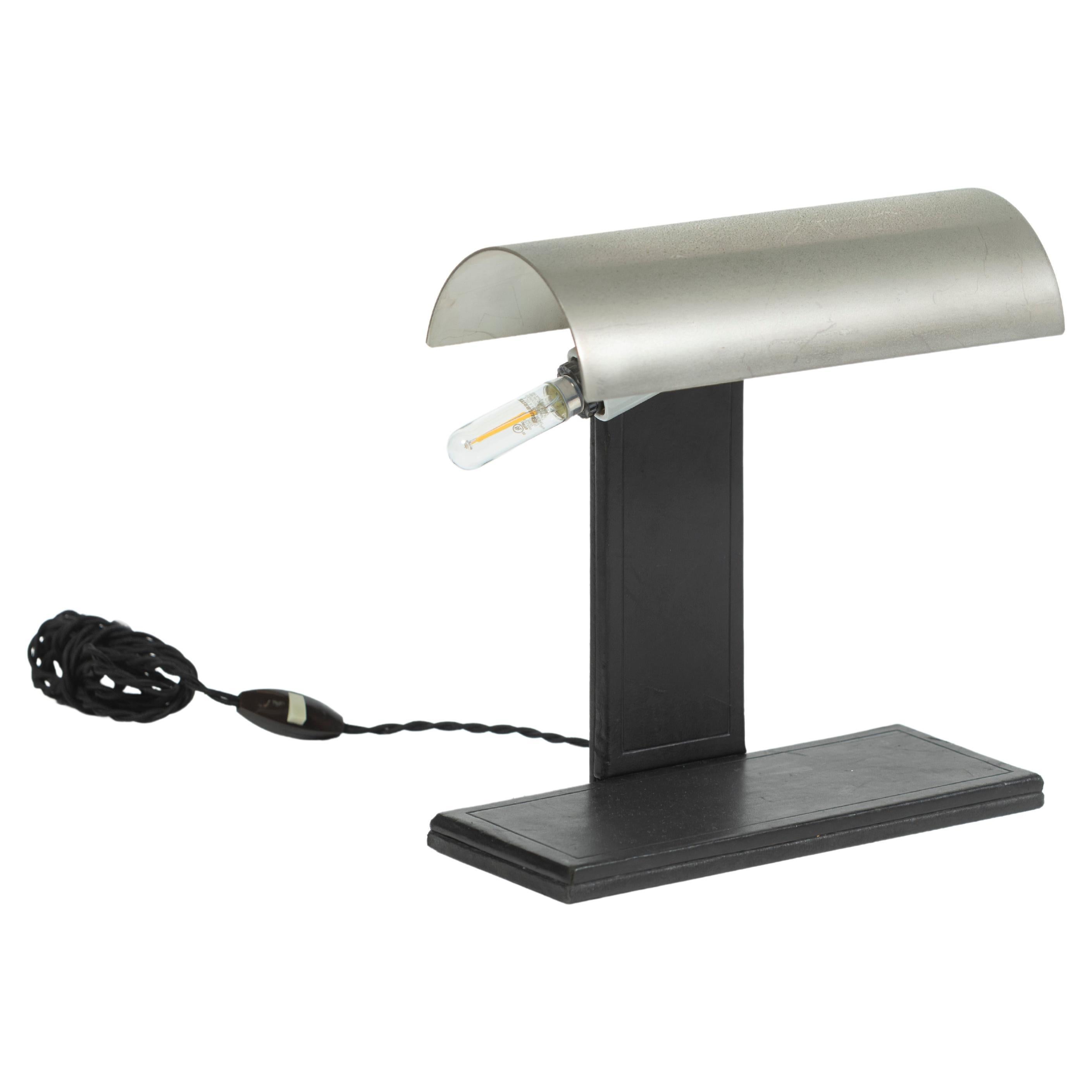 Highly collectible Art Moderne table lamp by Jacques Adnet, with neck nd base entirely wrapped in dark leather with a chrome shade. The fixture holds a pair of horizontal bulbs and is turned on/off on the cord. Great streamlined design for a desk or