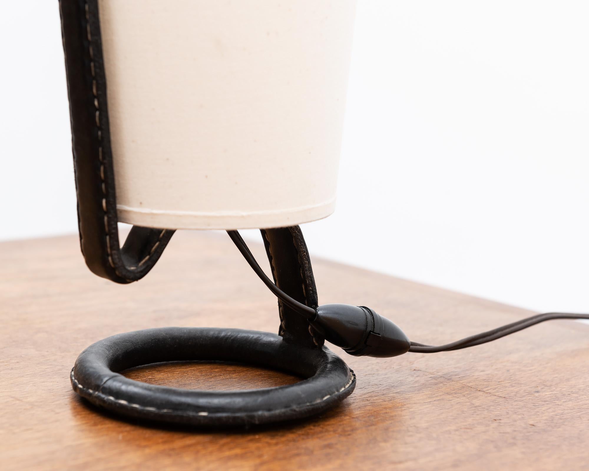 A handsome table lamp by Jacques Adnet in stitched black leather with linen shade. With original toggle cord switch, France, 1950s.