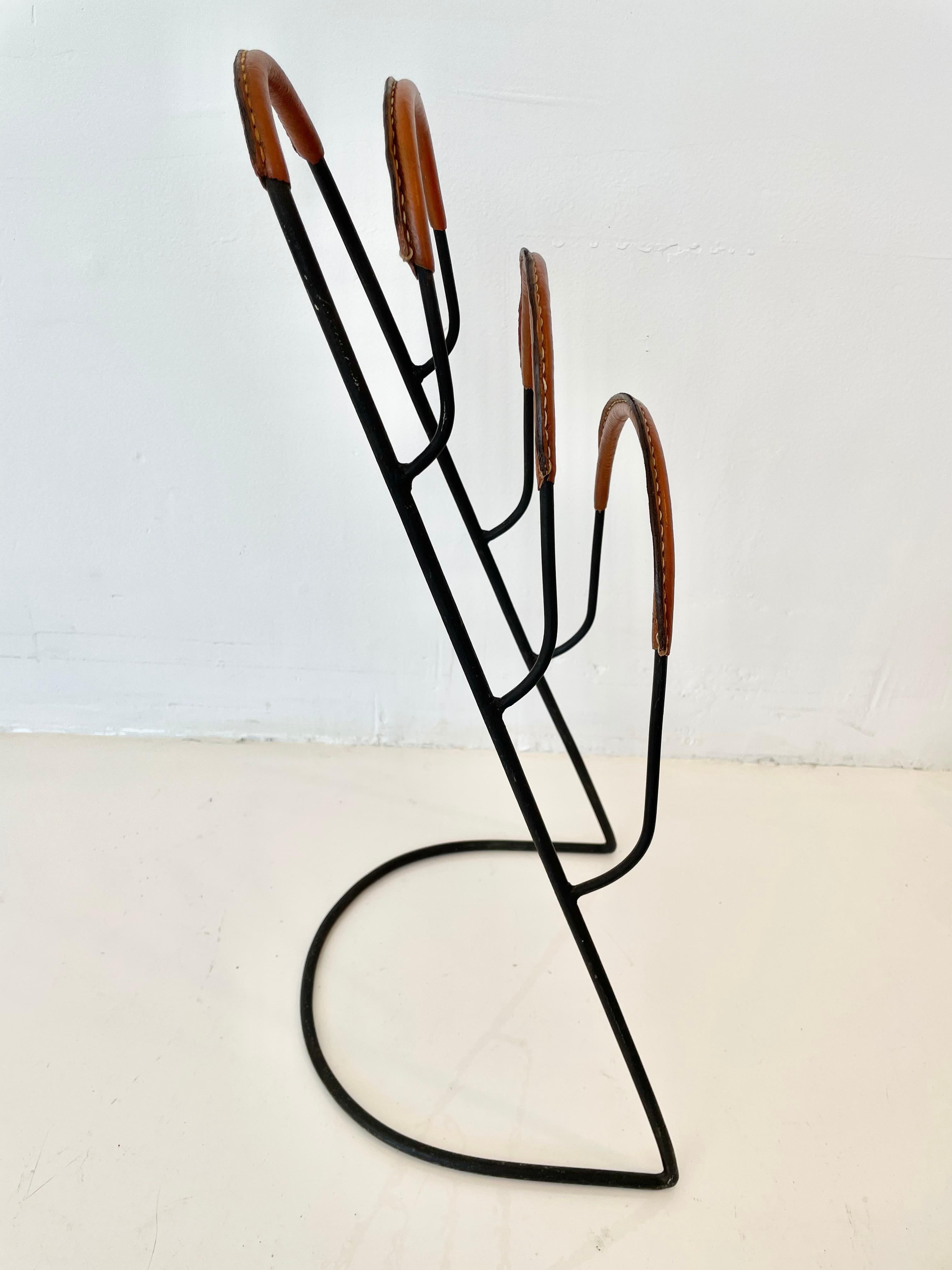 Very unusual vertical magazine rack by French designer Jacques Adnet. Iron frame with leather wrapped handle and trays. Three angled metal trays to hold magazines or books. Great sculptural piece and excellent example of collectible Adnet design.