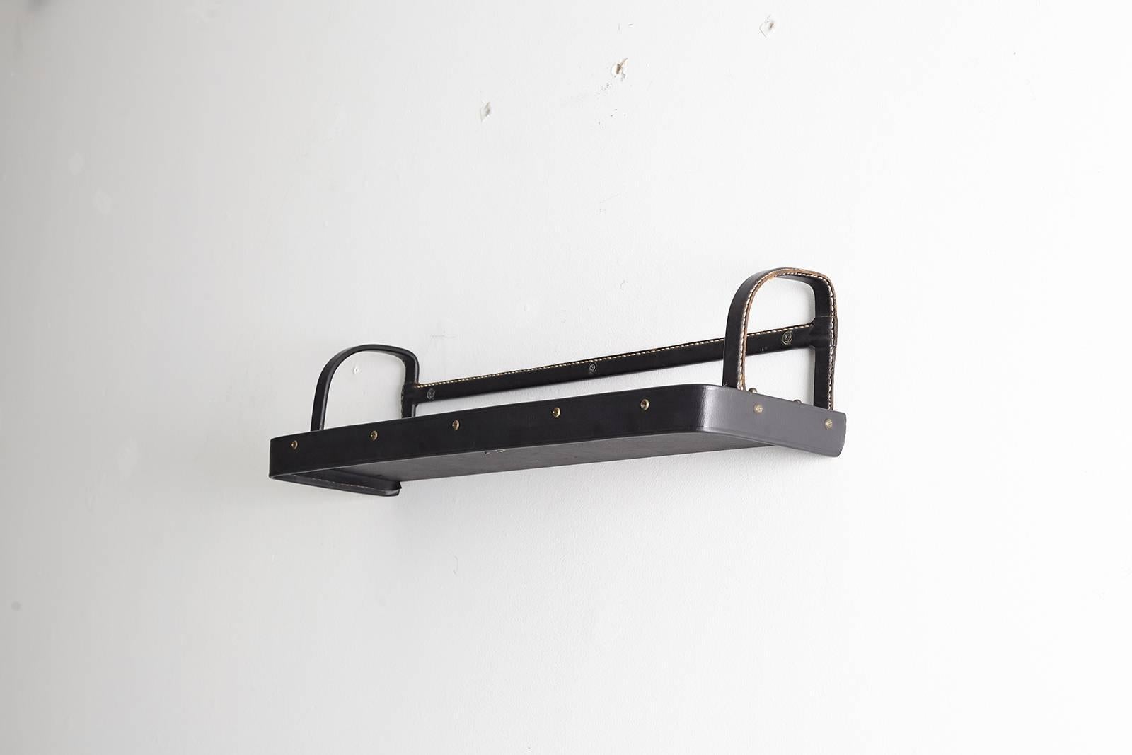 Handsome wall shelf and book holder by Jacques Adnet. Black leather and white contrast stitching with brass hardware. Nice age and patina to leather.