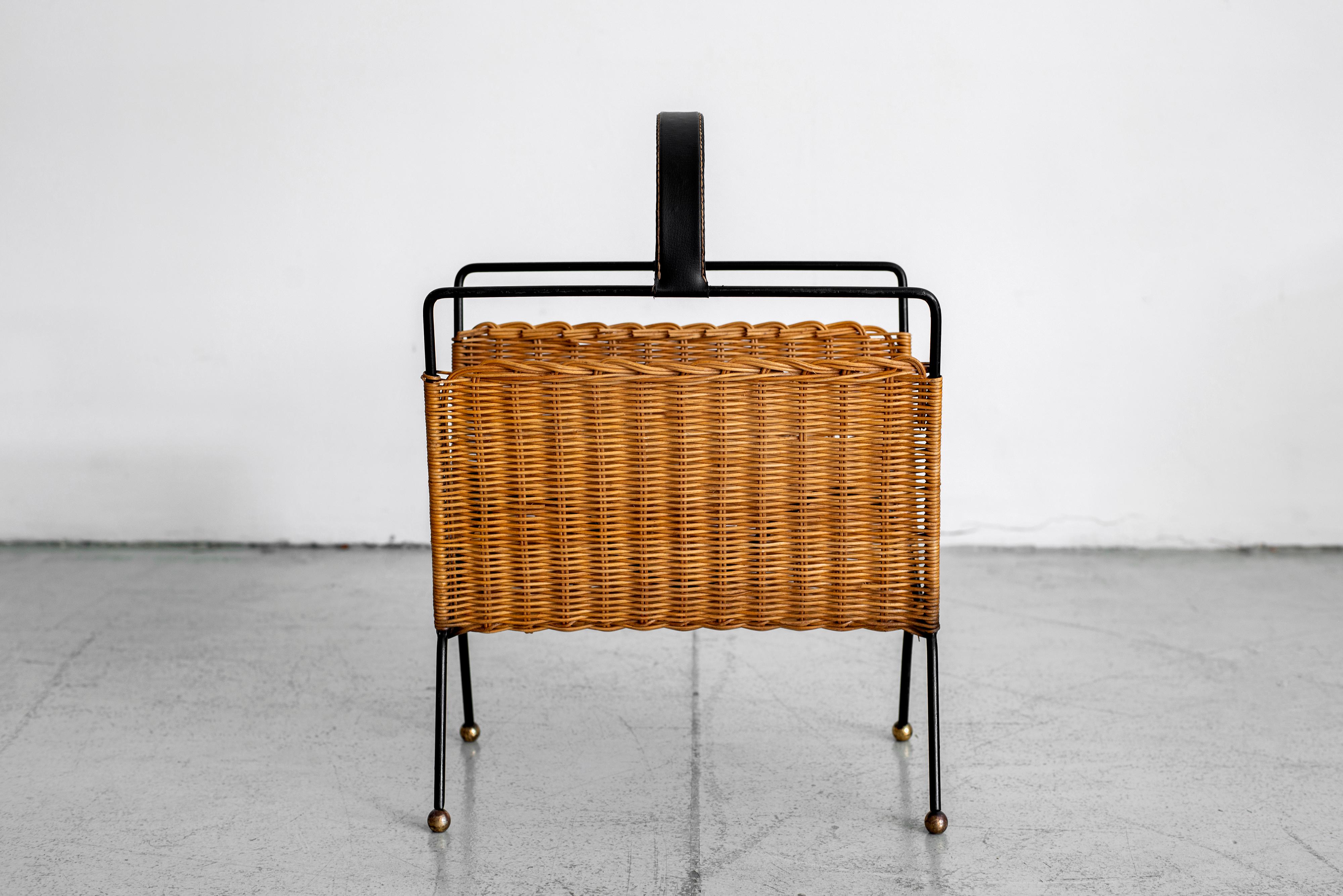 Unique Jacques Adnet wicker magazine rack with black iron frame and handle, woven wicker sides, and brass ball feet.