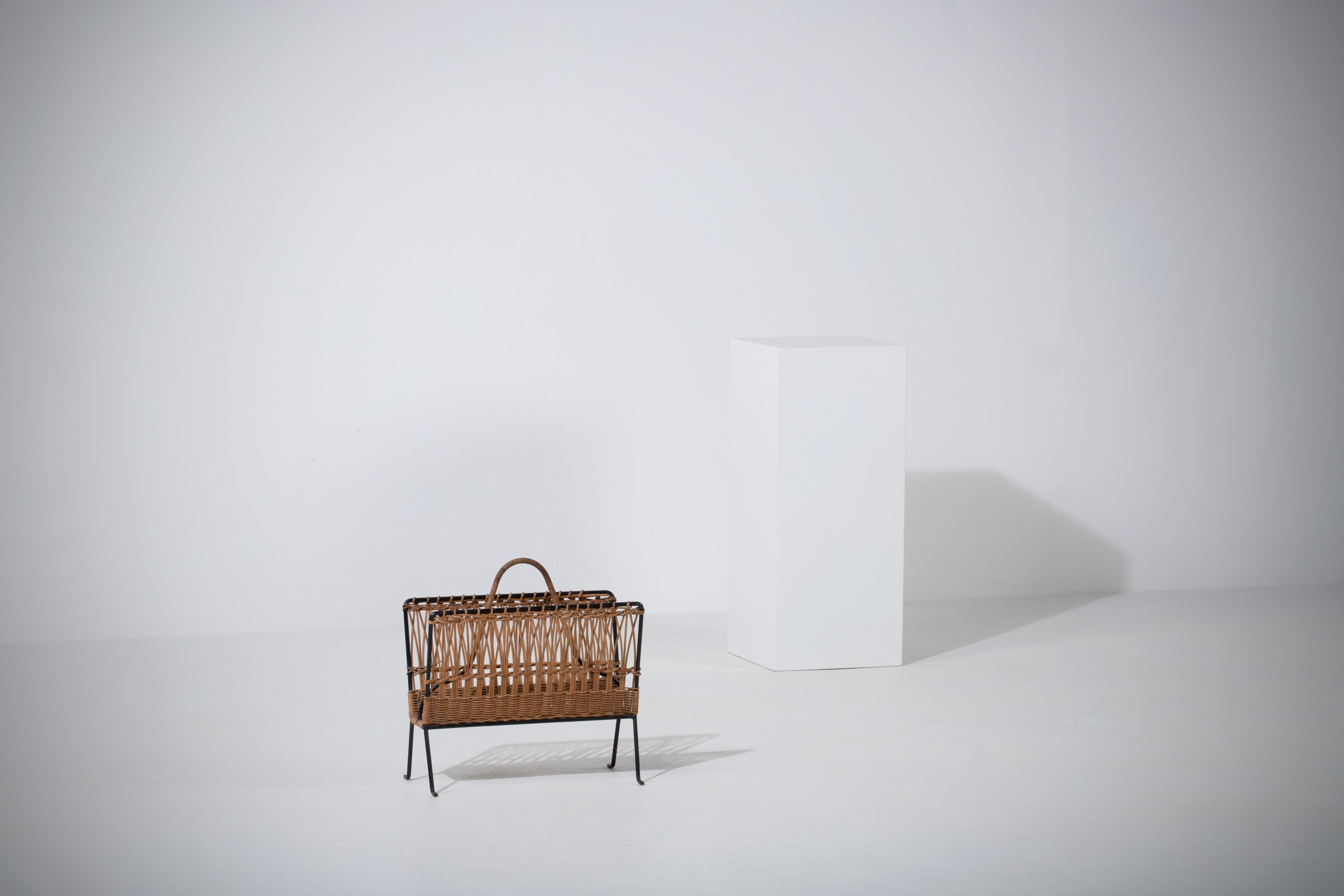 Introducing a truly unique Jacques Adnet wicker magazine rack, a perfect blend of style and functionality. This rare piece features a sturdy black iron frame, elegantly woven wicker sides, and a practical handle for easy mobility. 

This