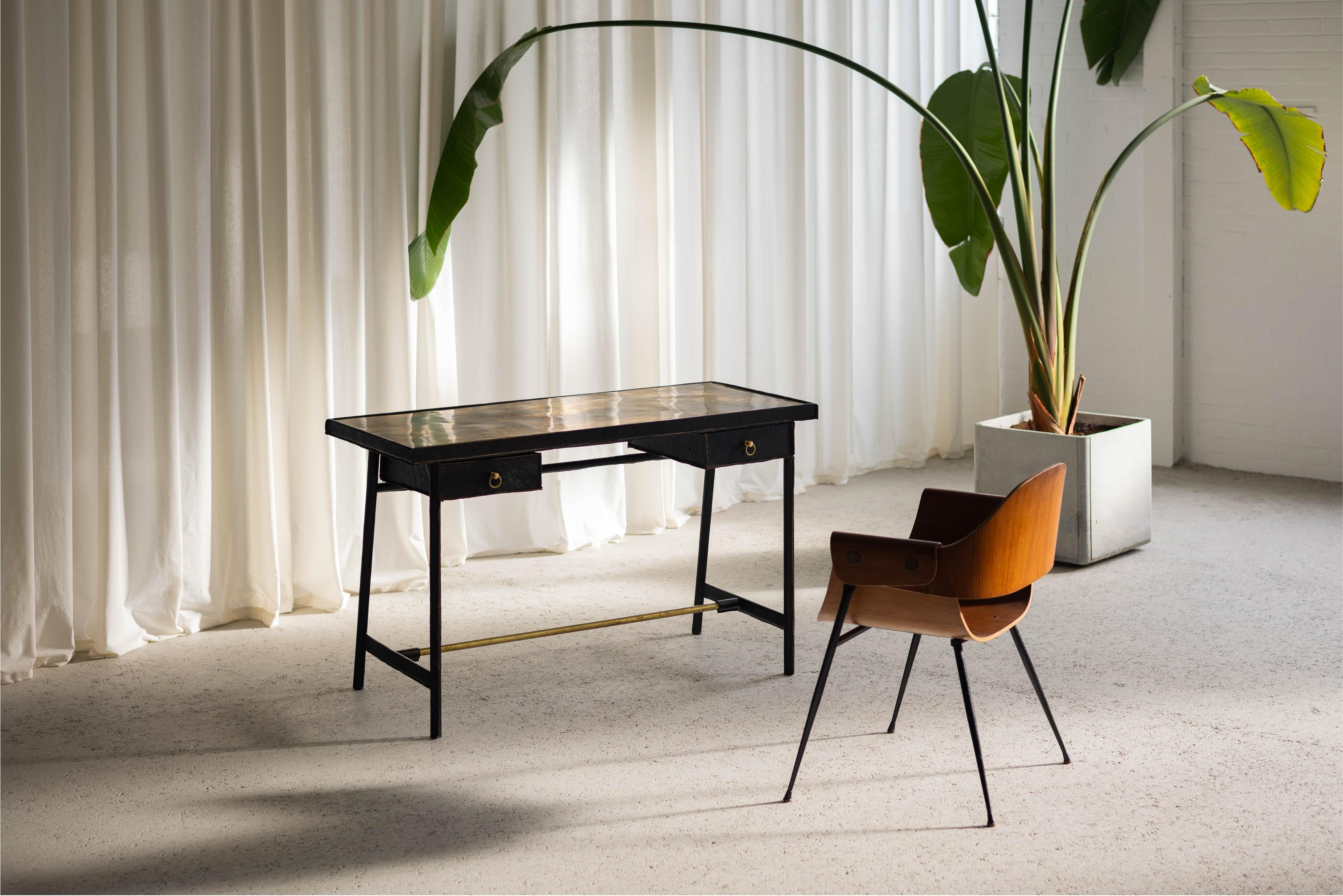 This stunning avant-garde desk, designed by Jacques Adnet and crafted in his own atelier in France during the 1950s, is a masterful blend of luxury and innovation. The frame is fashioned from solid brass, wrapped in rich black leather that exudes