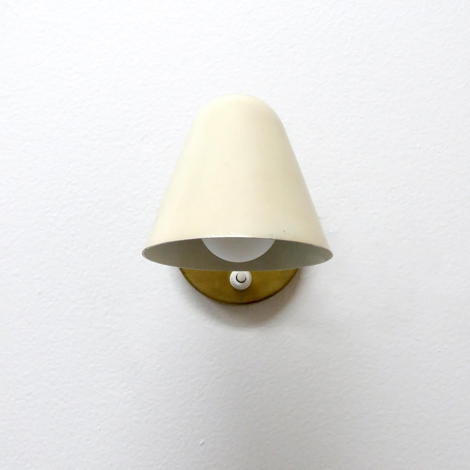 Elegant, petite Jacques Biny wall light, in brass with wonderful egg shell enameled shade, original back plate with individual light switch, mounted on ball joint for full shade rotation, wired for US standards, one E12 socket, max. wattage 60w or