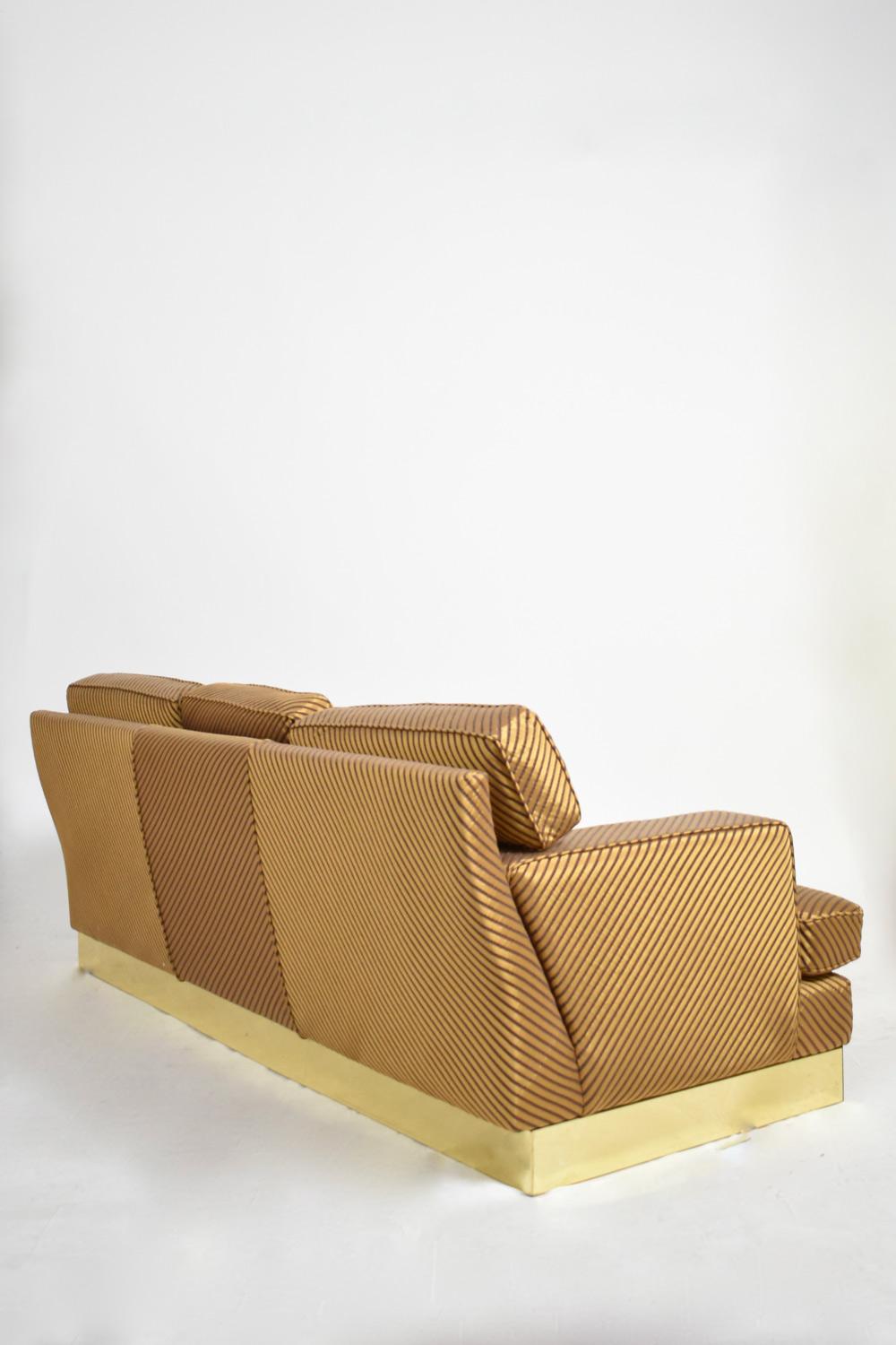Comfortable sofa in the style of Jacques Charpentier resting on a brass-plated plinth, upholstered with a gold and brown stripes fabric. France, 1970s.