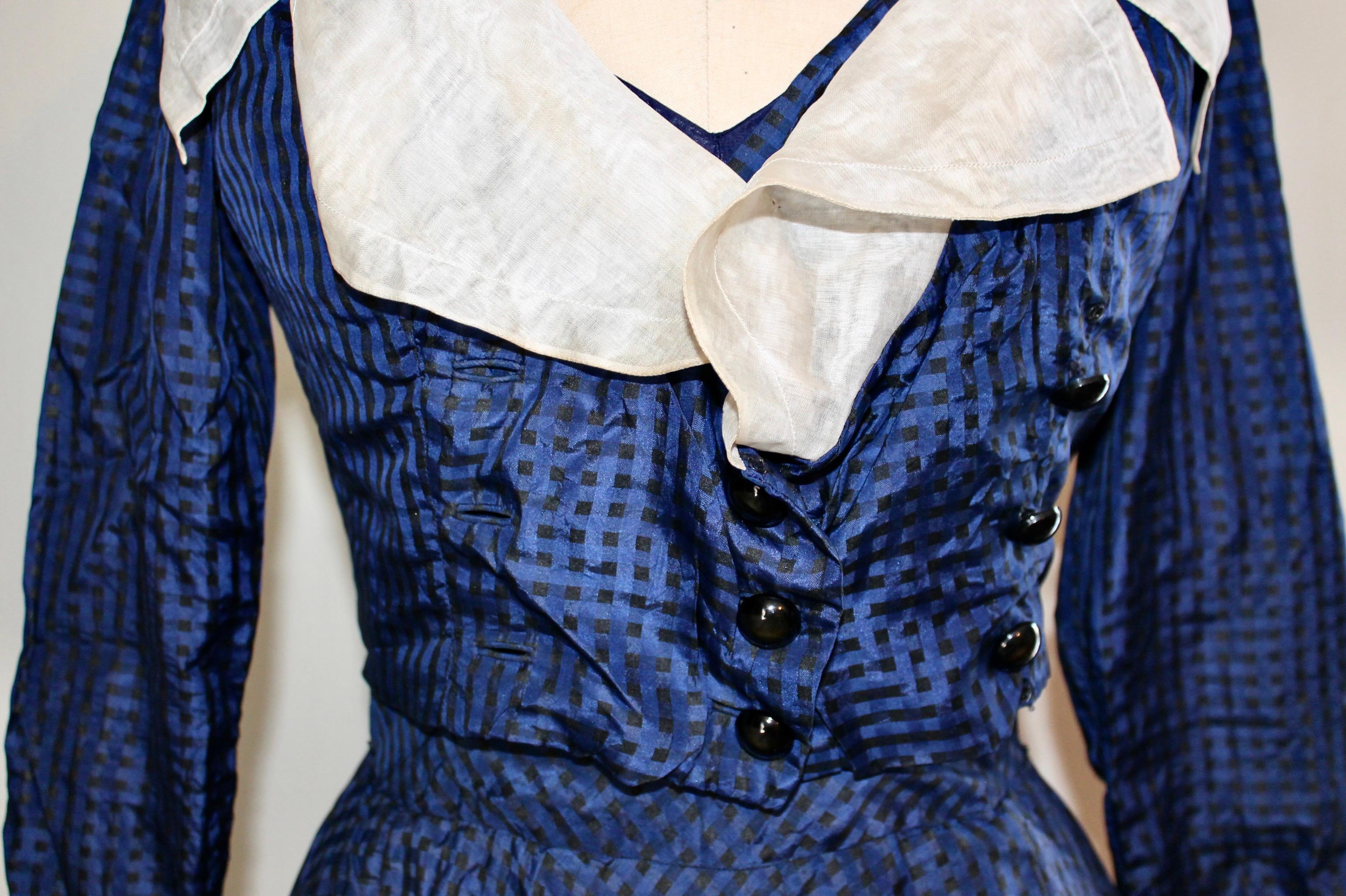 Cobalt Blue checkered silk taffeta dress and jacket.  Jacket has collar of organza and attached organza bow ties on the sleeves. Blue slip appears to be synthetic fabric. The skirt is lined with (possibly) paper thin organza.  The Label reads: