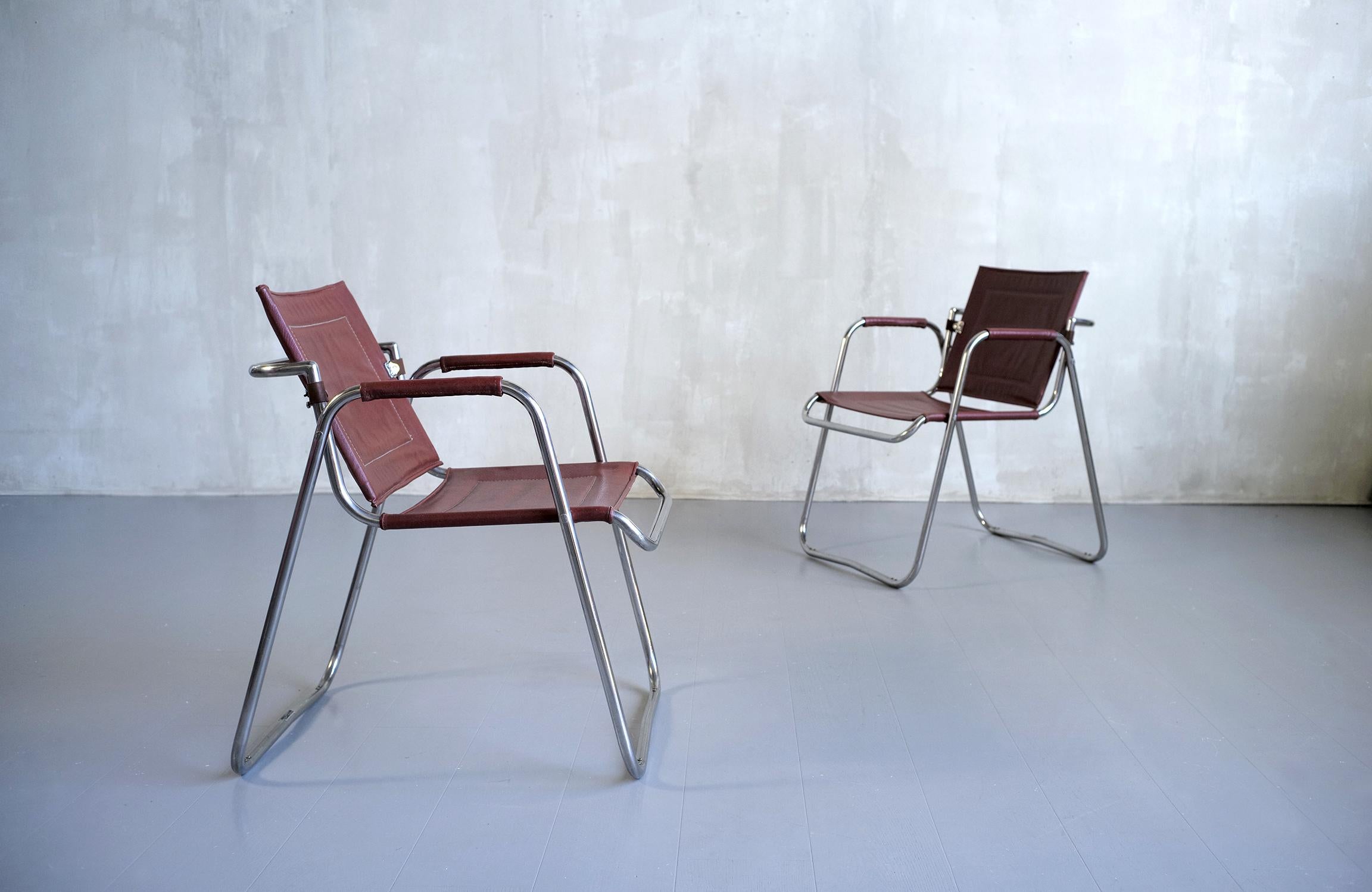 Paire de fauteuils en métal tubulaire nickelé créés par Jacques Hitier, produits par Tubauto dans les années 1950. Le siège, les accoudoirs et le dossier sont recouverts de leur similicuir bordeaux d'origine. Le dossier est pivotant et muni
