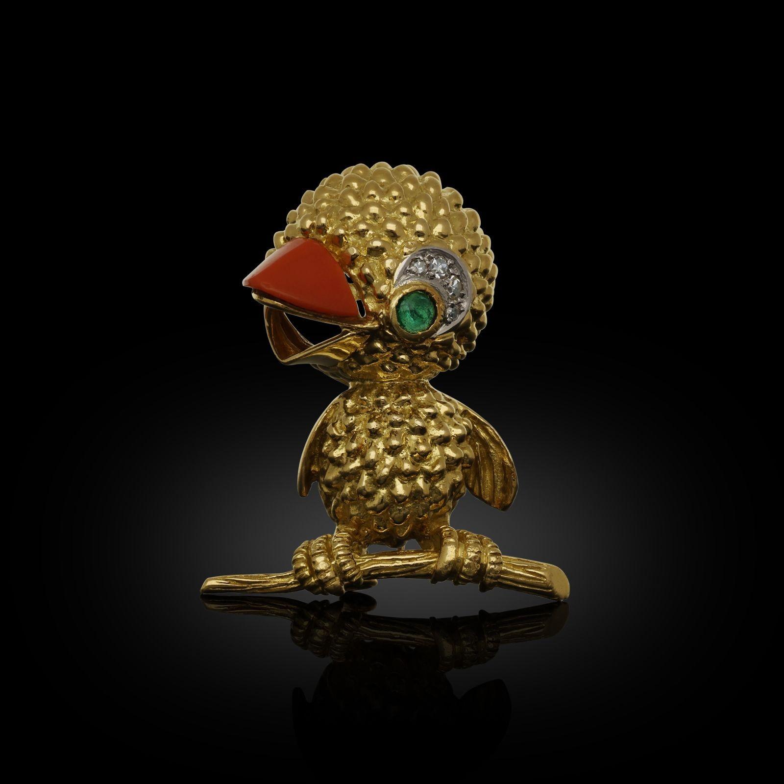 A charming gold and gem-set chick brooch by Jacques Lacloche c. 1950s, the chick depicted standing on a branch, the body in heavily textured 18ct yellow gold, the open beak set with a piece of polished coral, the eye with an emerald cabochon and