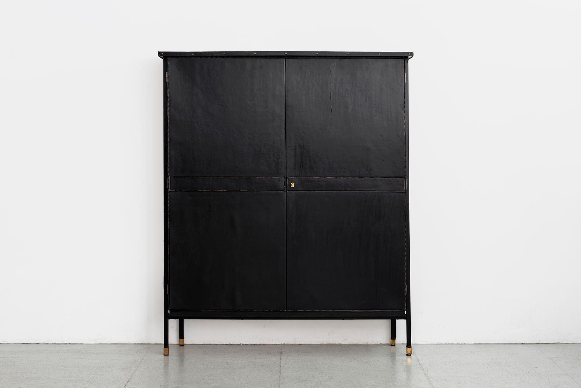 Incredible wardrobe armoire by Jacques Quinet, circa 1950s
Covered in black leather with saddle stitching, opens with two solid doors to reveal fixed shelving interiors. 
Wonderful brass hardware and brass feet. 
Extraordinary piece. 

 