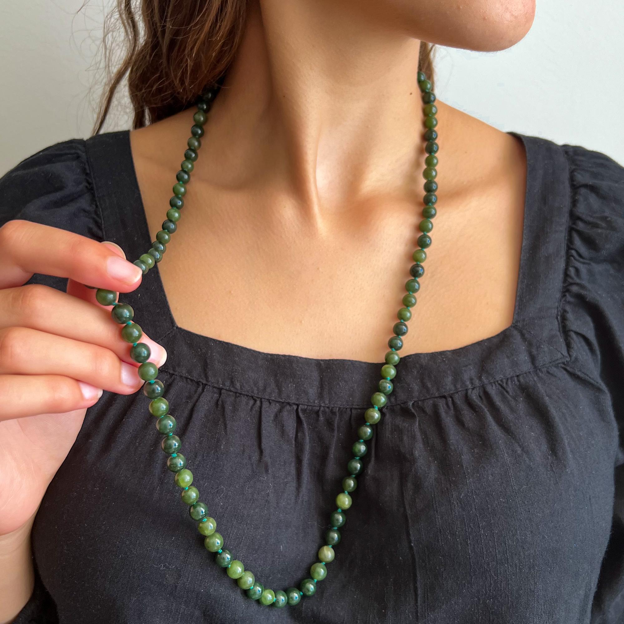 A vintage jade single-strand beaded necklace set with a gold ribbed ball clasp. The jade beads of this necklace are round-shaped and beautifully mottled with different hues of dark green. Between the beads the green thread is knotted, this ensures