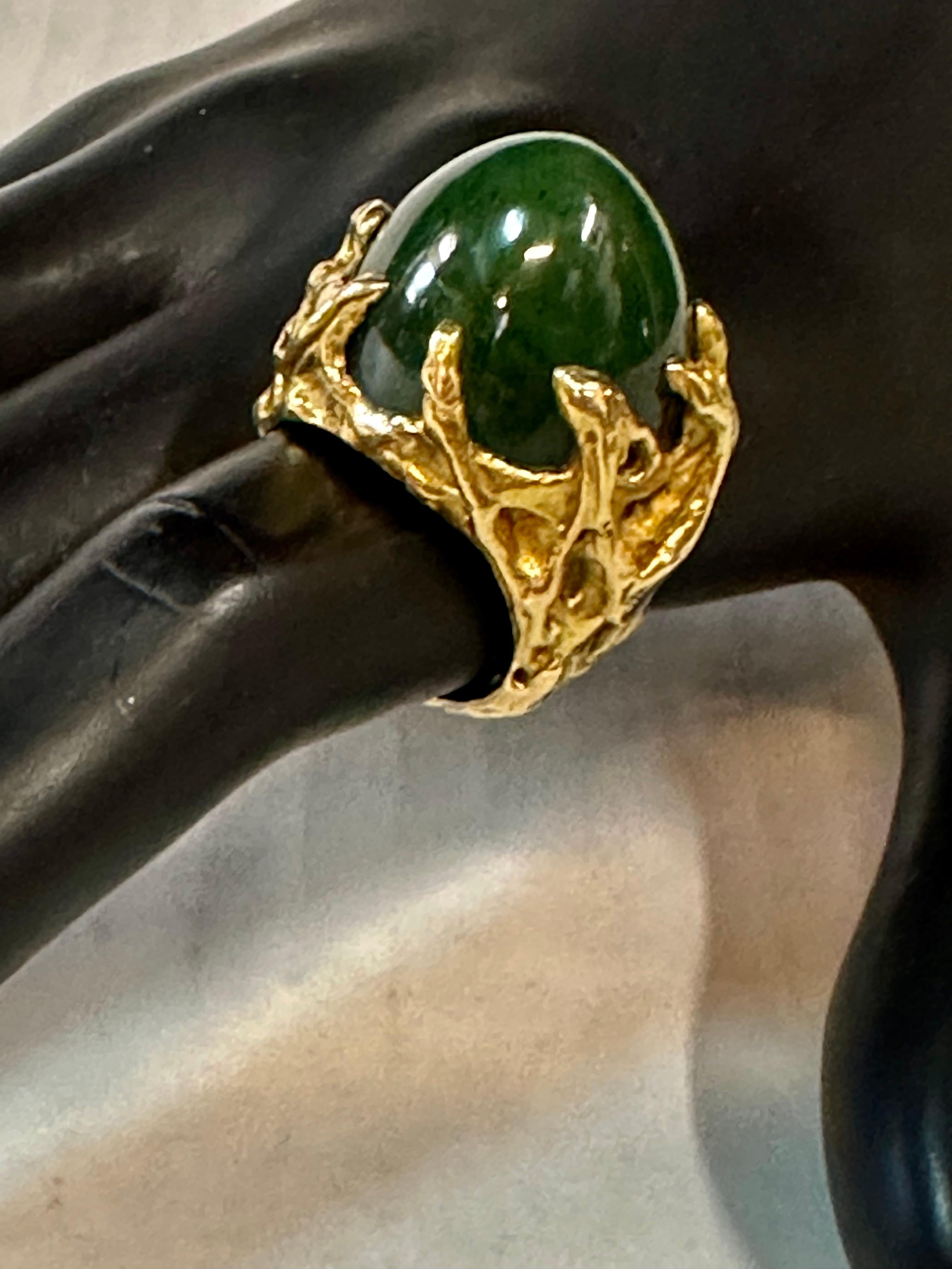 Cette impressionnante bague en or 18 carats et en jade a été conçue et fabriquée sur mesure par les bijoutiers Merrin de New York dans les années 1960. Elle présente une spectaculaire monture sculptée avec un énorme jade vert foncé en forme de dôme.
