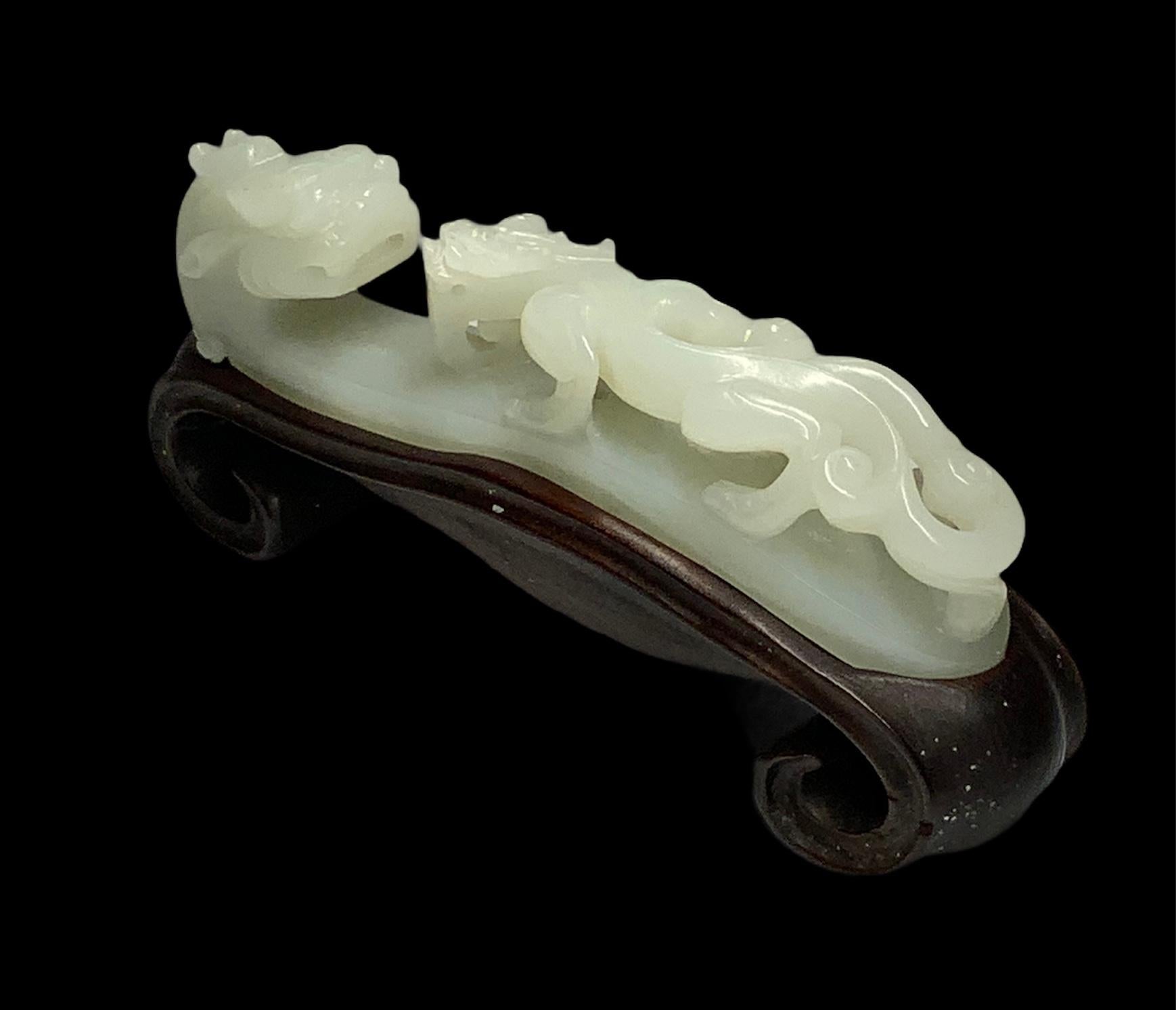 This is a Jade carving of a dragon head facing a leopard. This leopard is walking over the body of the dragon. Both figures stand over a chinese scroll wood base. In Chinese culture the leopard symbolizes the taming of cruelty. The dragon symbolizes