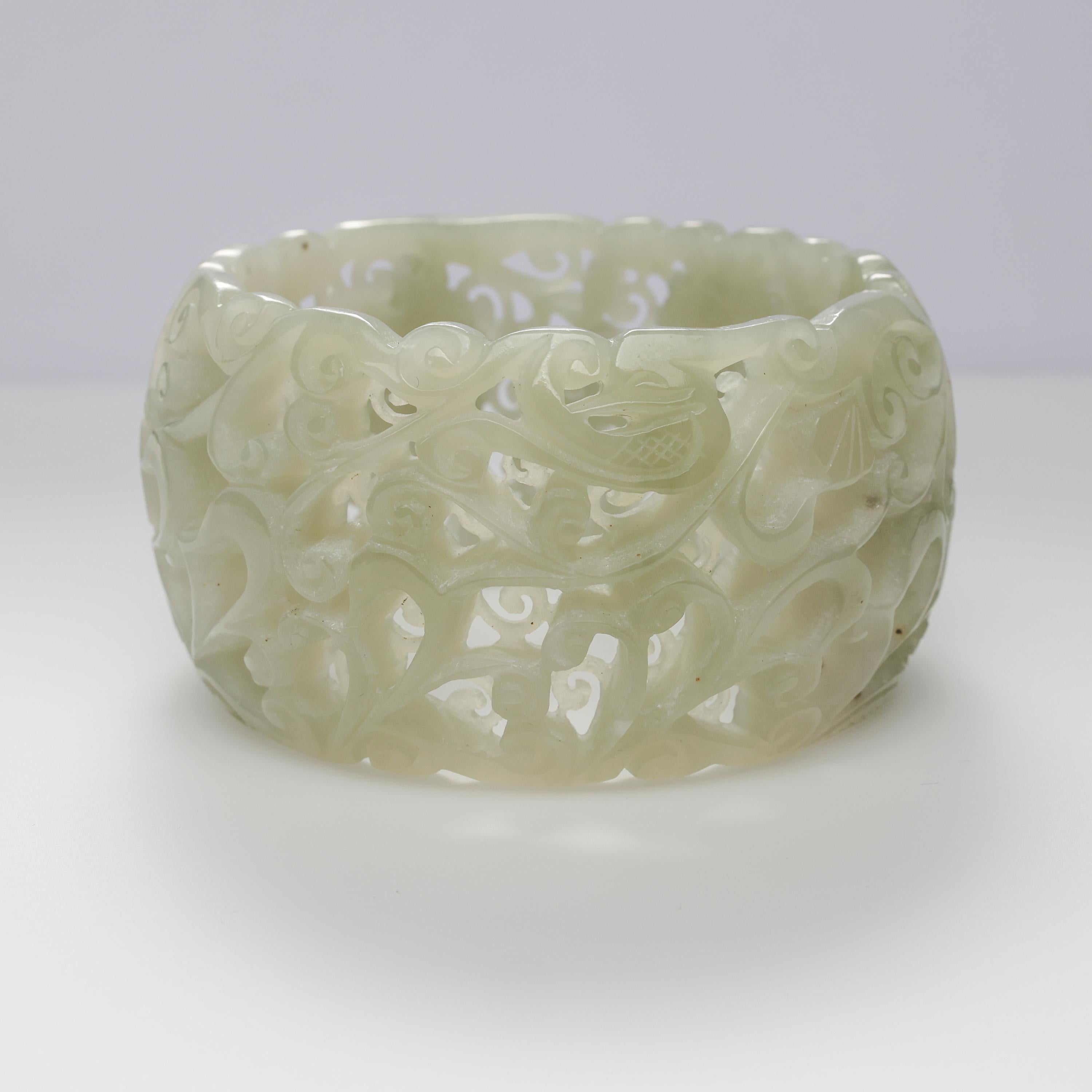 This large white nephrite jade bangle is simply astonishing. Expressively -and intricately- hand-carved and pierced with leaves, blossoms, ruyi mushrooms, and decorative leaves and swirls, the 43mm wide cuff is carved in two laters: the outer layer