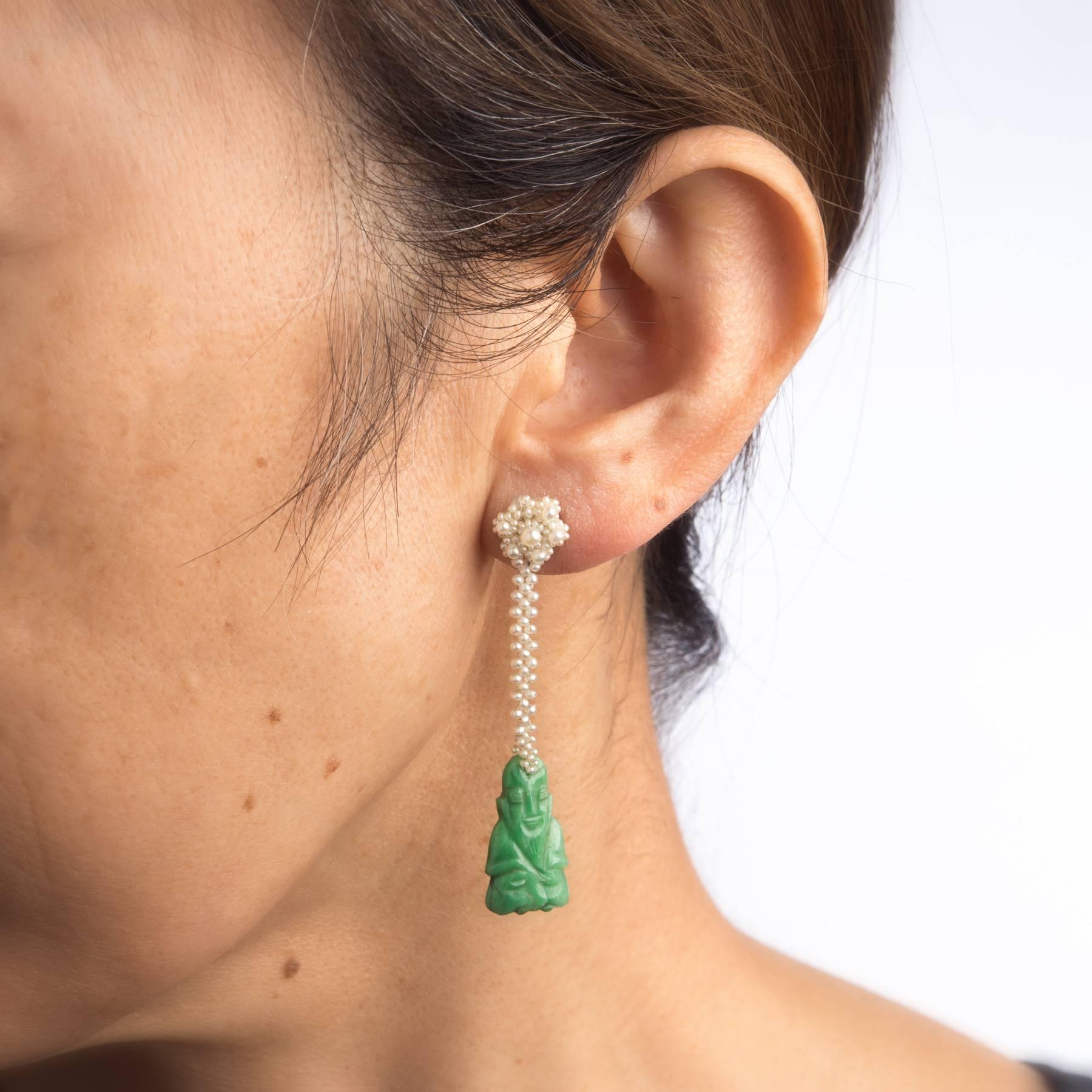 Overview:

Finely detailed pair of vintage drop earrings (circa 1950s to 1960s), crafted in 18k white gold. 

Jade is carved in the form of a Buddha and measures 19mm x 12mm, accented with seed pearls woven into a floral display (upper). The jade is
