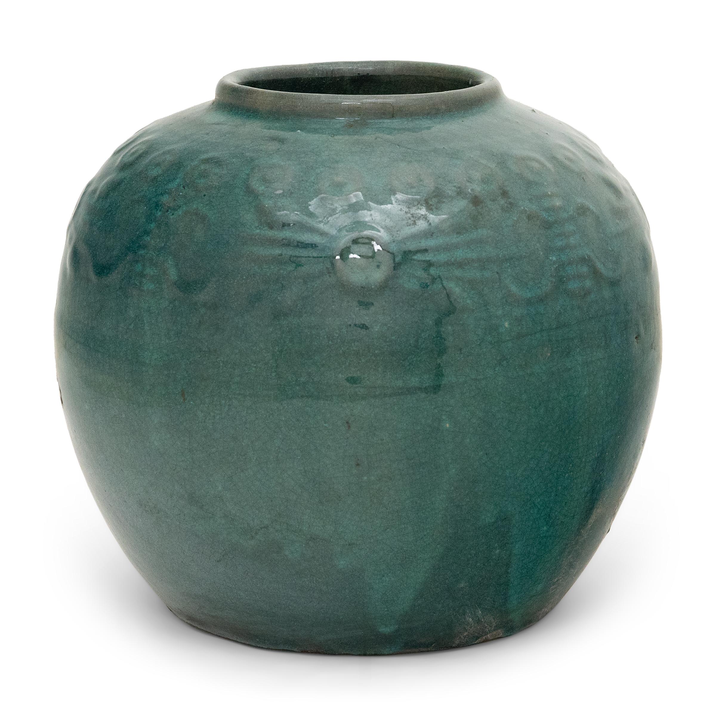A glassy, blue-green glaze gracefully drips across the rounded body of this provincial kitchen pot, lingering beautifully on the low relief decoration to the jar's shoulders. Among the raised patterns are round chrysanthemum blossoms and stylized