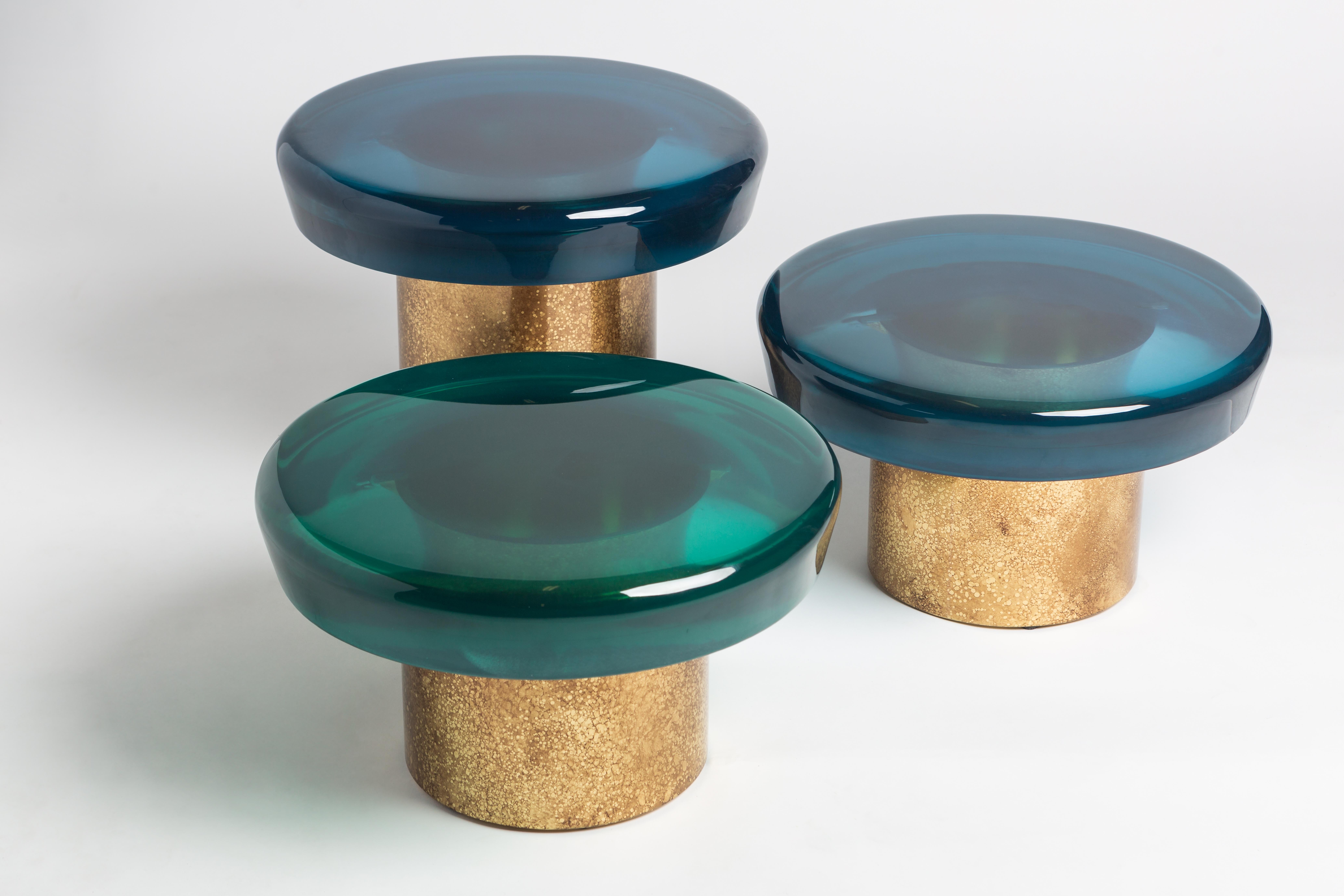La table basse Jade se caractérise par une transparence éthérée et une surface réfléchissante qui joue naturellement avec la lumière. Le plateau de table aux couleurs vives repose sur une base cylindrique en laiton, dont les veines distinctives sont
