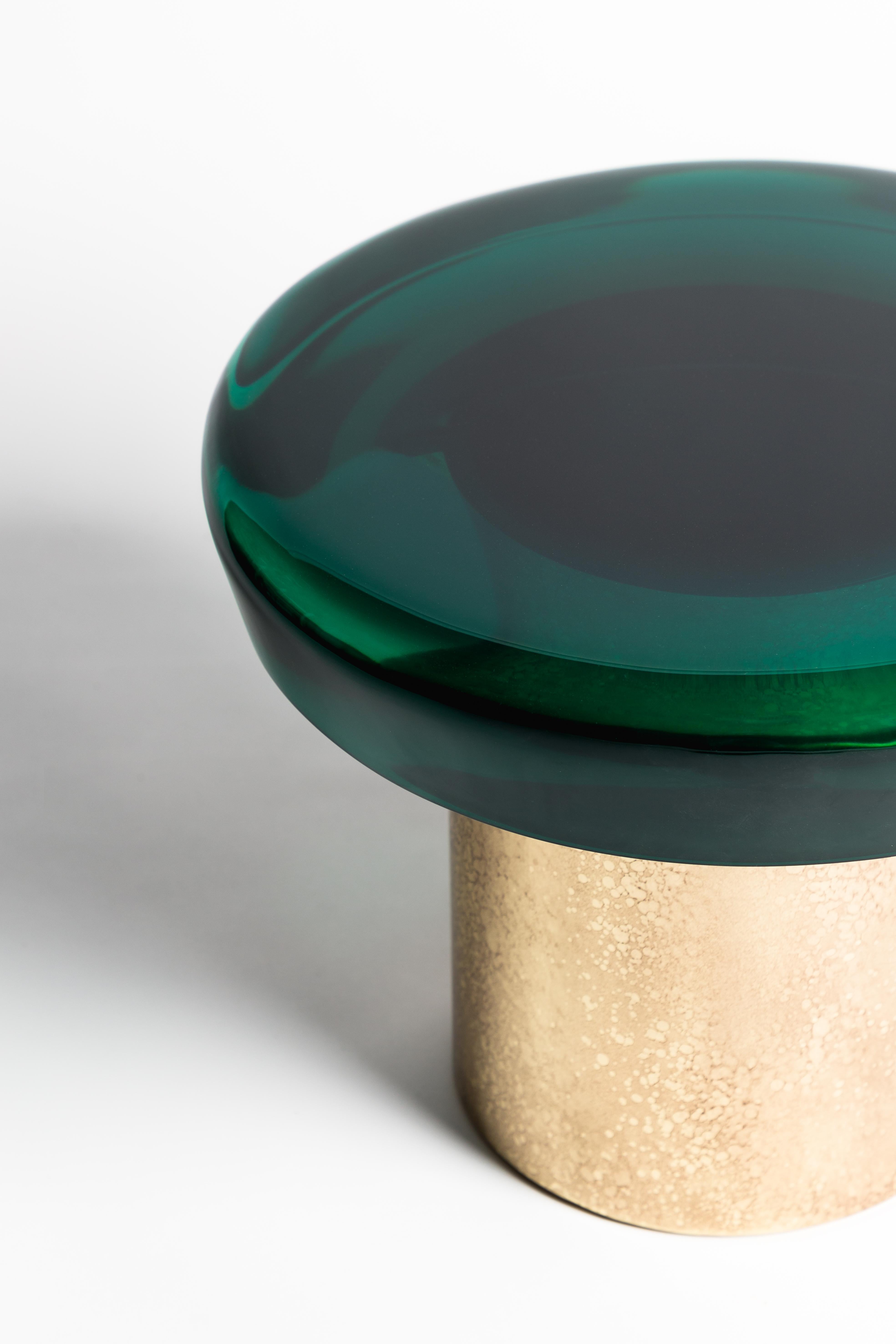 This coffee table resembles a precious gem, showcasing an otherworldly translucency, a lavish tactile quality, and a reflective finish that poetically interacts with light. The resin tabletop is set upon a brass frame with distinctive veining,