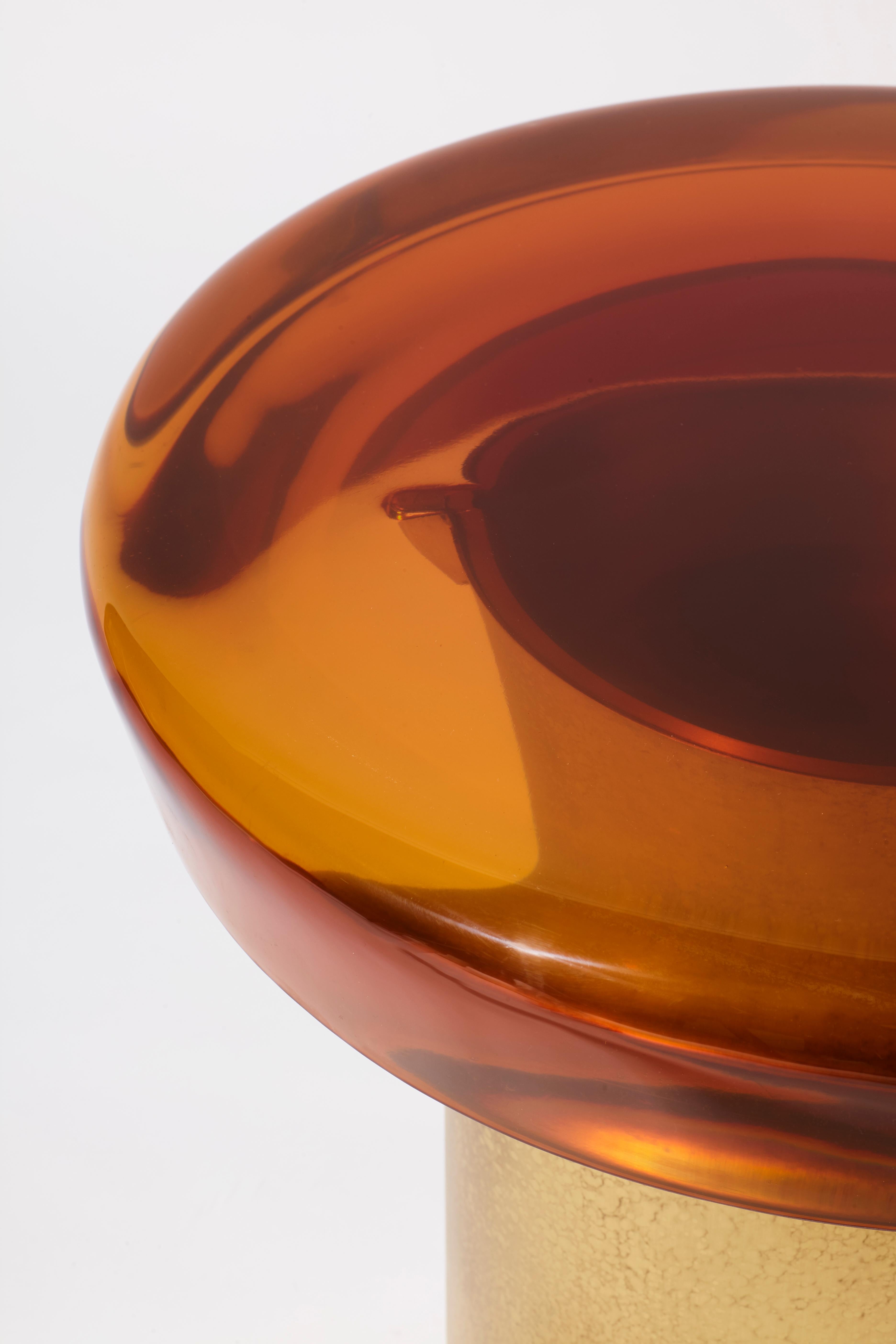 Il tavolino Jade è caratterizzato da una trasparenza eterea e da una superficie riflettente che gioca naturalmente con la luce. Il piano del tavolo dai colori vivaci poggia su una base cilindrica in ottone, le cui caratteristiche venature sono