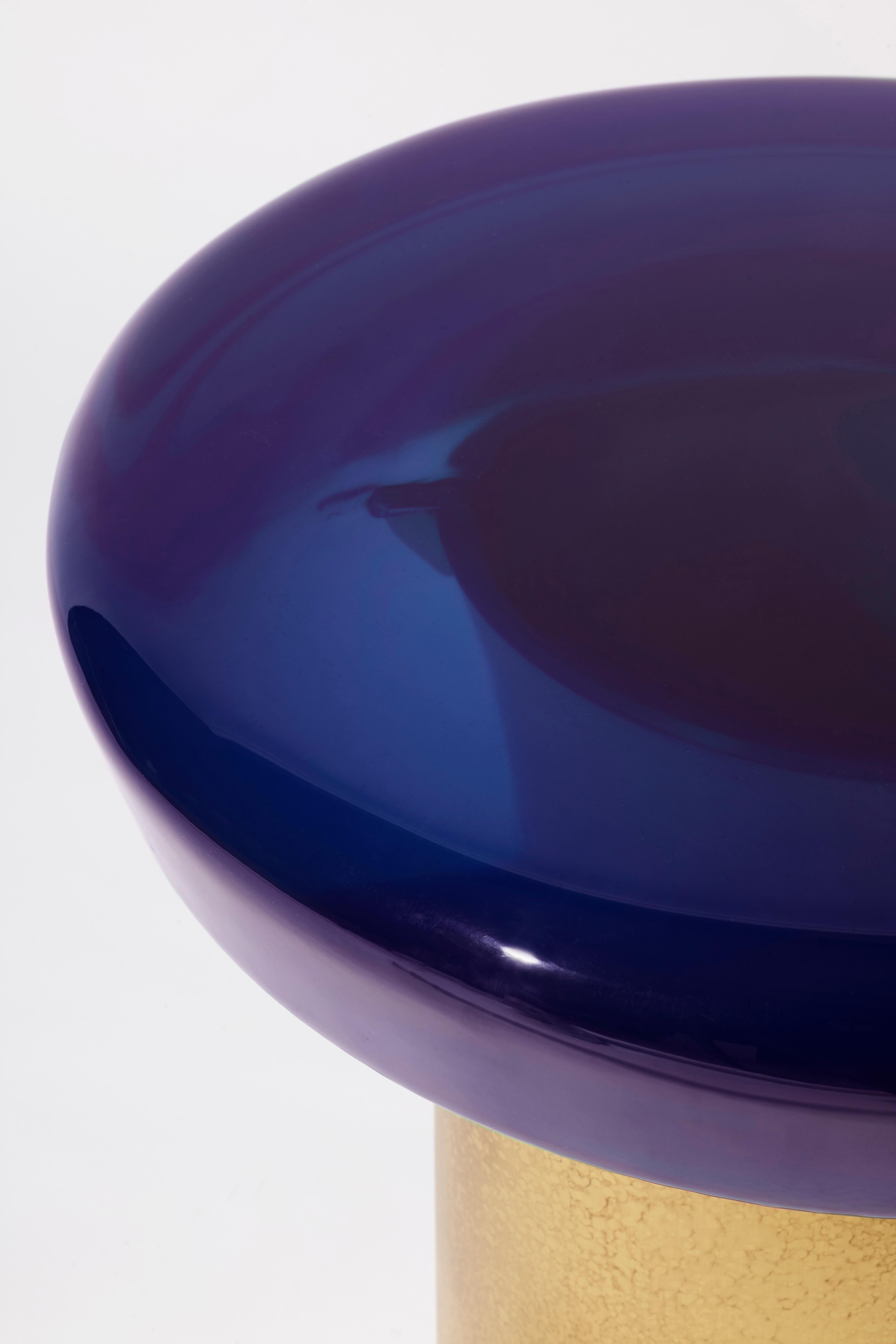 La table basse Jade se caractérise par une transparence éthérée et une surface réfléchissante qui joue naturellement avec la lumière. Le plateau de table aux couleurs vives repose sur une base cylindrique en laiton, dont les veines distinctives sont