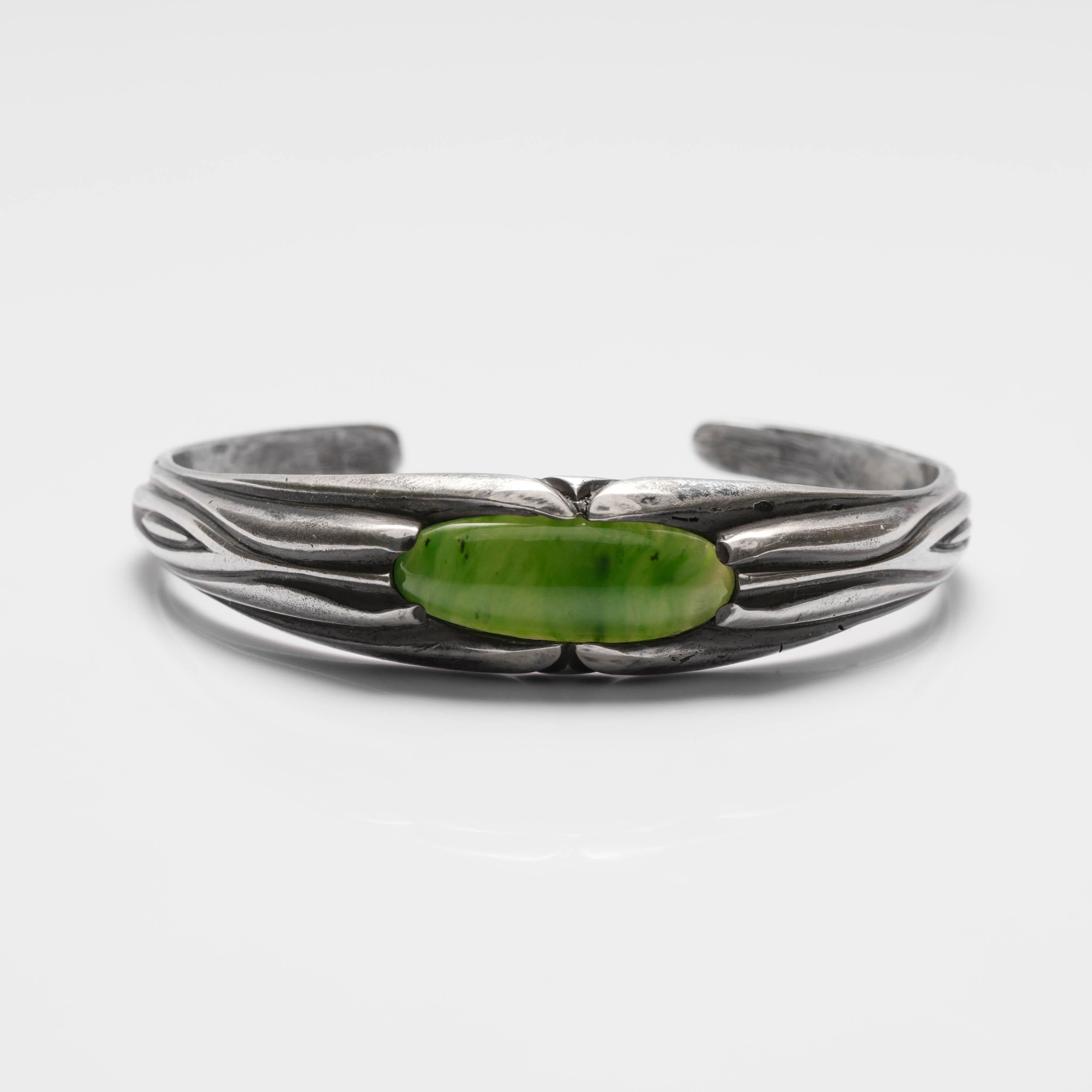 This handmade silver and jade bracelet was created by a master silversmith and features an oval cabochon of natural and untreated highly translucent nephrite jade. The cuff design makes the bracelet easy to slip on and off. It can be worn by anyone