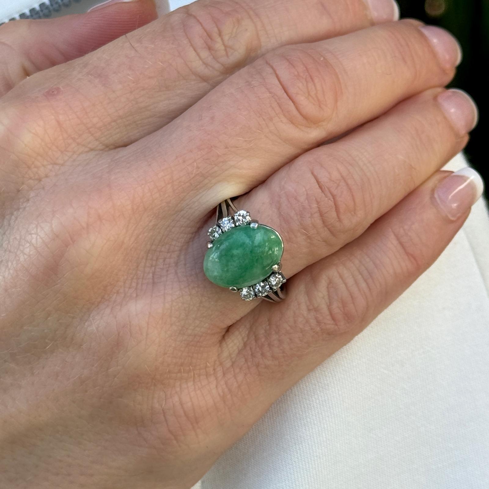 Green jade and diamond cocktail ring crafted in 18 karat white gold. The ring features a cabochon oval green jade gemstone flanked by 6 round briliant cut diamonds weighing approximately .33 carat total weight. The diamonds are graded G-H color and