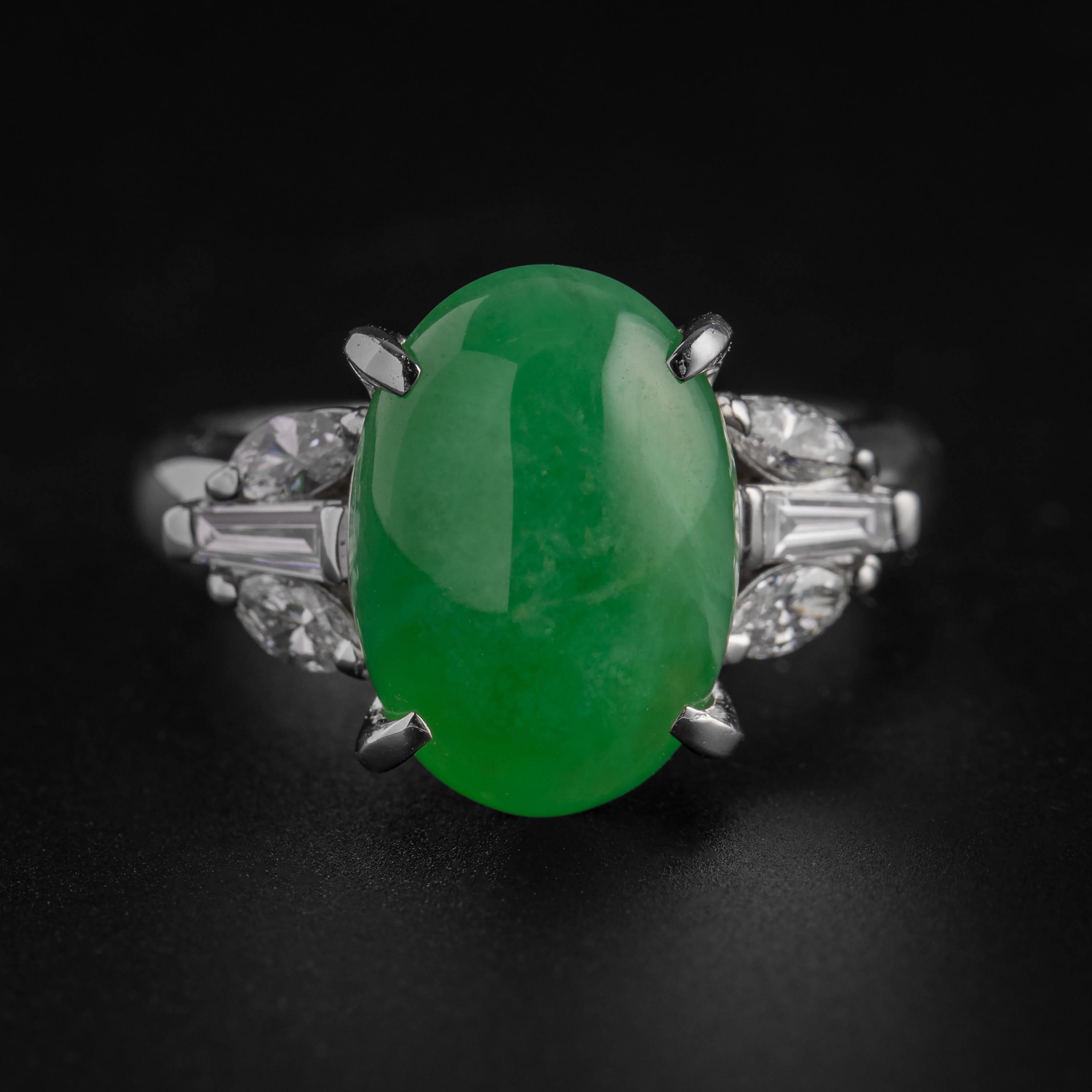 A gemmy apple green cabochon of certified natural, untreated Burmese jadeite is prong-set into a sleek platinum mounting and accompanied on both sides with a trio of fiery white diamonds —two marquise and one tapered baguette— in this stunning