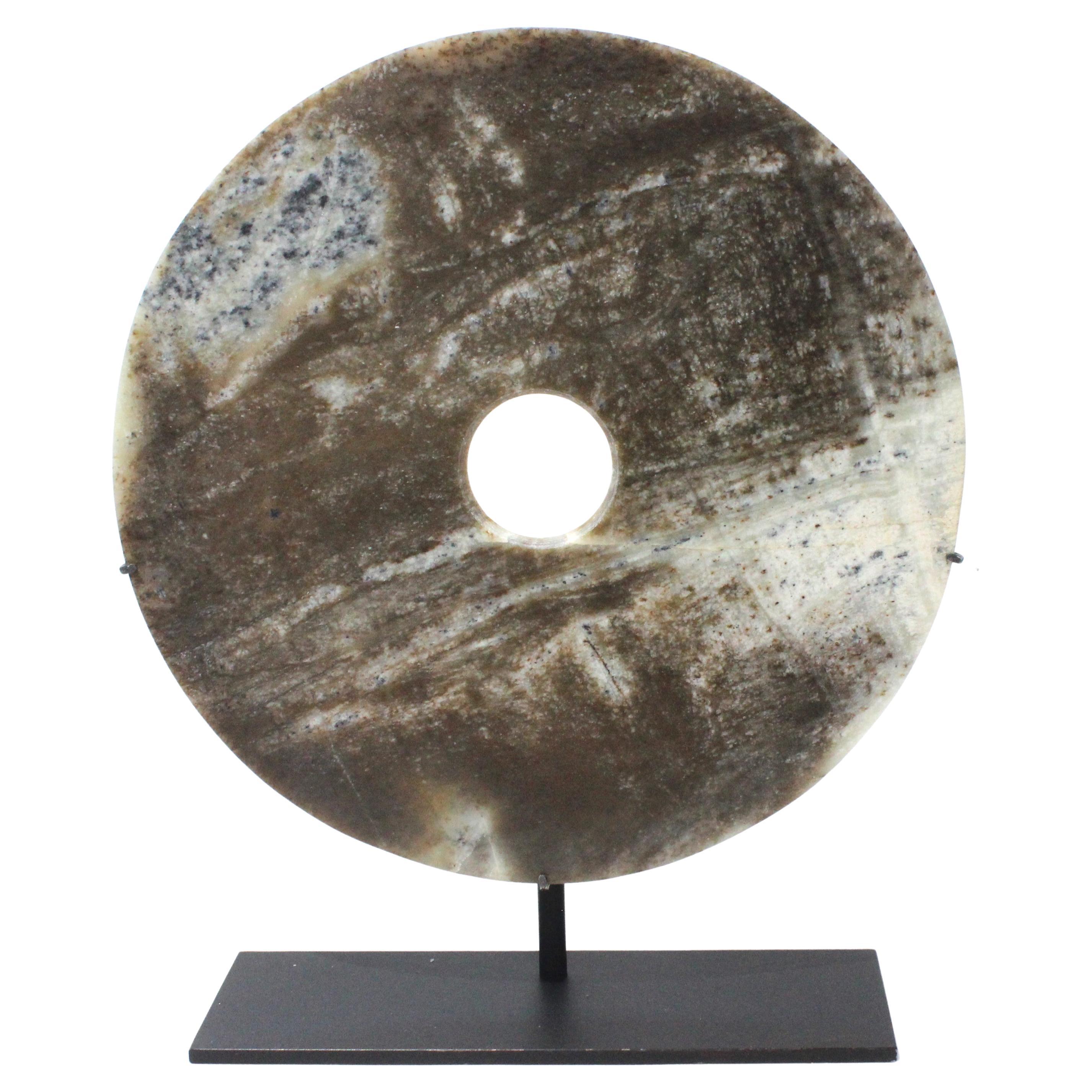 This stylish mounted jade disc will make a subtle statement with its form and use of materials. The stone has a mottled coloration of browns, charcoals, slate greens and antique creams. 

Note: overall dimensions are 15