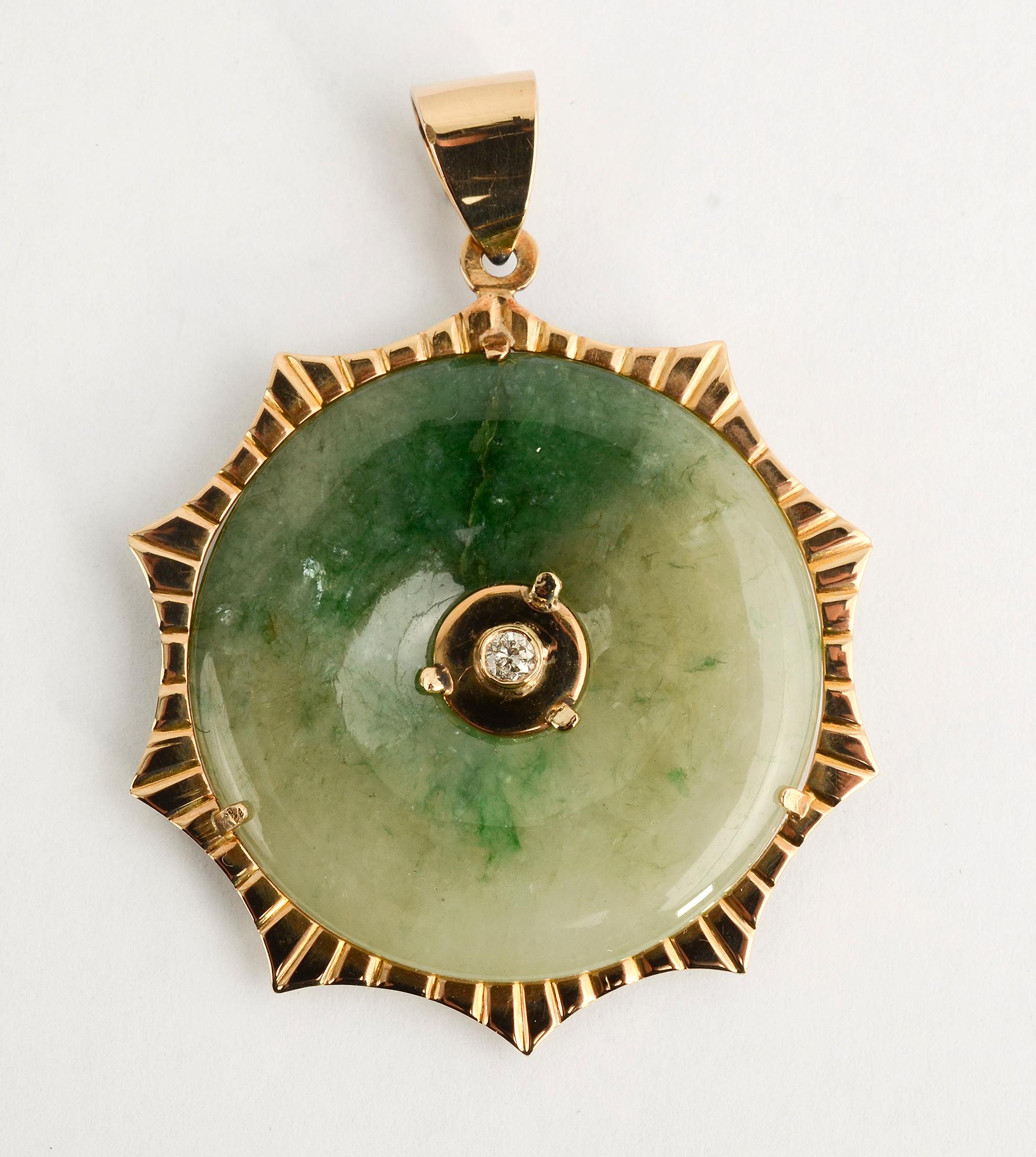 Lovely and unusual jade pendant centered with a diamond on each side. The diamonds are each approximately 1/5 carat. The jade is encircled by a gold frame with a slight sunburst design.
The pendant measures 1 3/4 inches in diameter. By